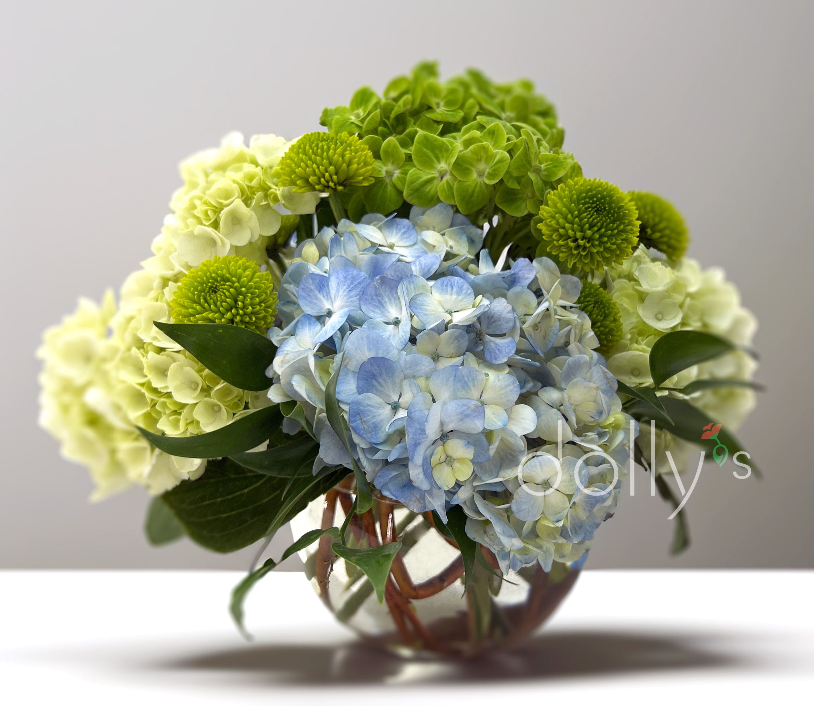 Delight  - Add a touch of elegance with a floral arrangement featuring blue and white hydrangeas accented with green mums.