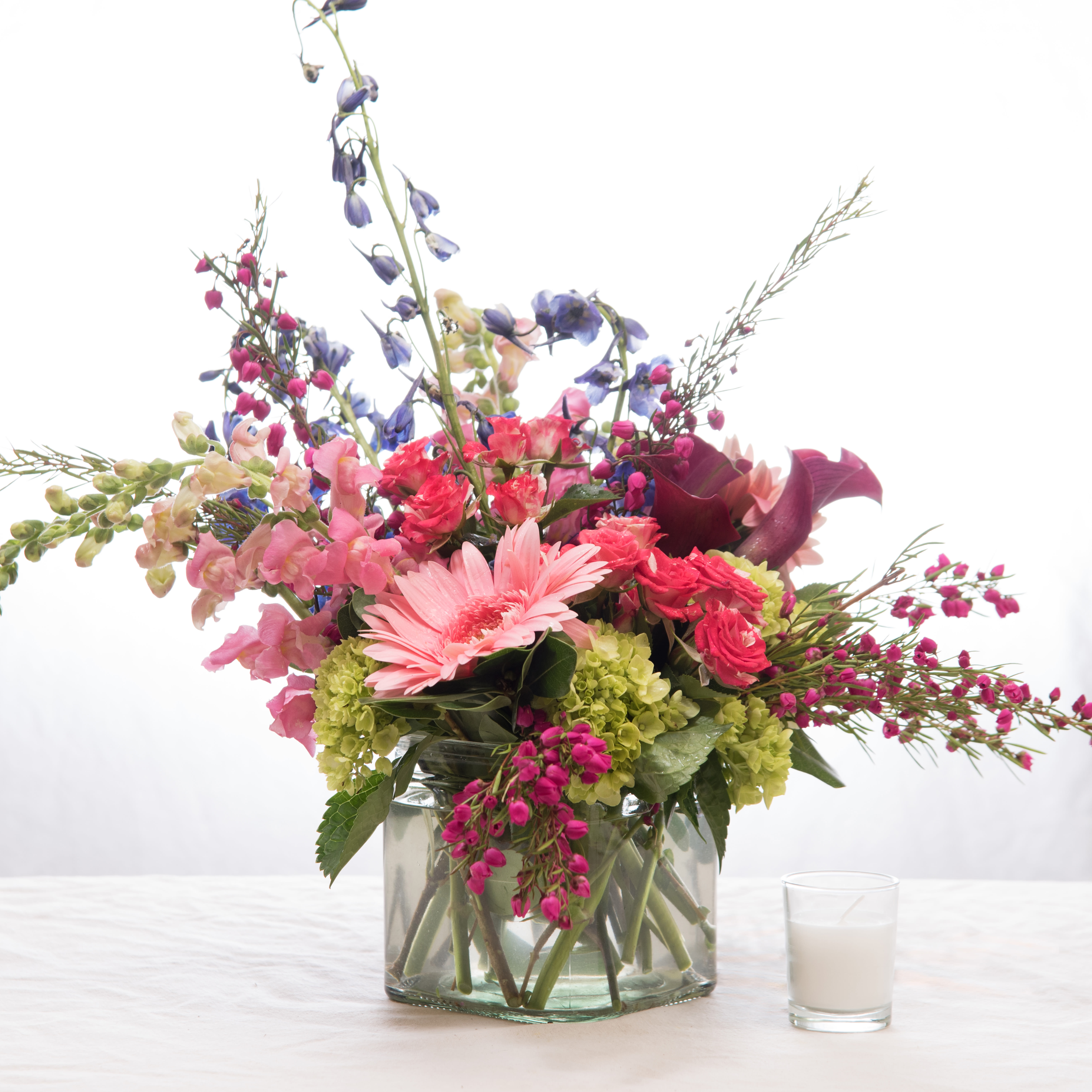 Burst of Spring - Gerbera daisies, mini calla lilies, spray roses, snap, and delphinium shooting out of a glass cube vase!