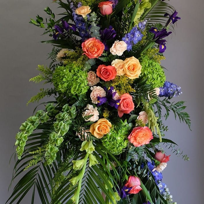 Cheerful Farewell Spray - This Cheerful Farewell Standing Spray is a true celebration of life. Bursting with a vibrant mix of colorful carnations, delicate roses, striking irises, elegant hybrid delphinium, fresh bells of Ireland, and lush hydrangea, this arrangement truly captures the spirit of the departed. The addition of verdant greenery adds texture and depth to this stunning display. Standing approximately 3' by 4', this standing spray is a beautiful and fitting tribute to honor the memory of a beloved friend or family member.