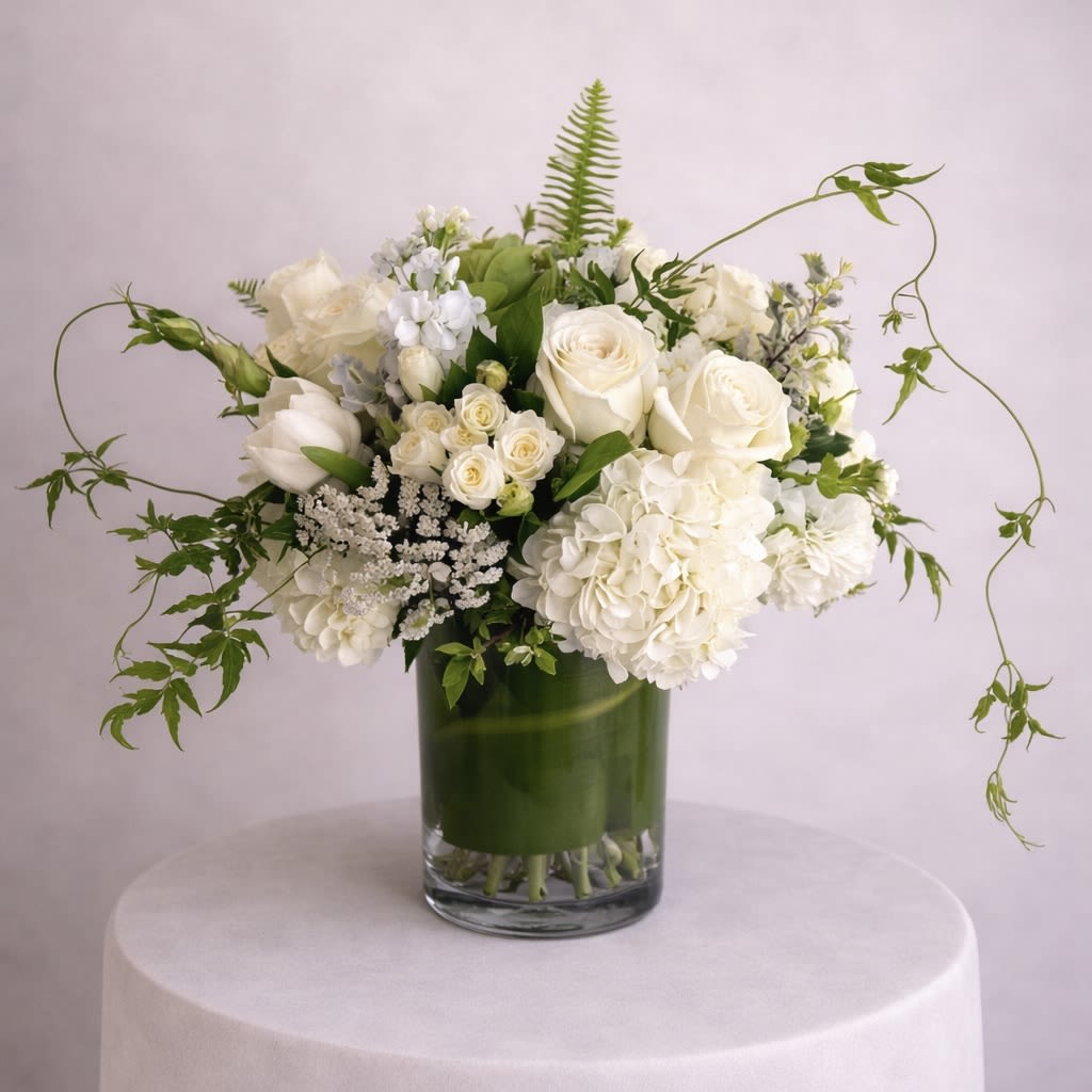 The Celtic - Elegance and simplicity come together in this stunning clear cylinder vase arrangement. White blooms accented with a delicate green ribbon create a timeless and versatile gift that is perfect for any occasion. Measuring approximately 12 inches tall by 8 inches wide, this arrangement is sure to make a statement.