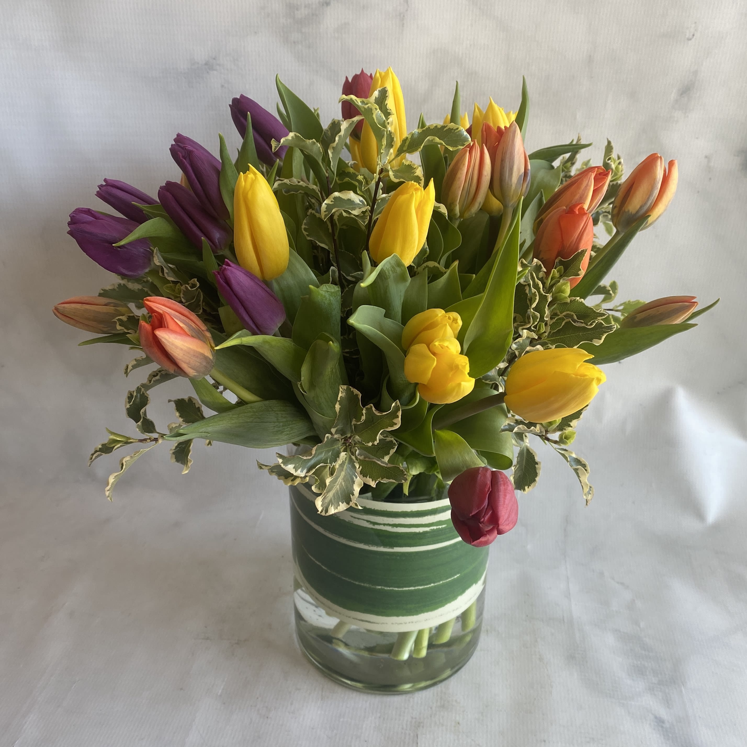 Bundle of Tulips - Indulge in the beauty of tulips with this stunning arrangement that's perfect for any tulip lover! Featuring an assortment of colorful tulips and delicate filler flowers, this arrangement measures approximately 10 inches wide and 12 inches tall, making it a perfect size for a desk or side table.