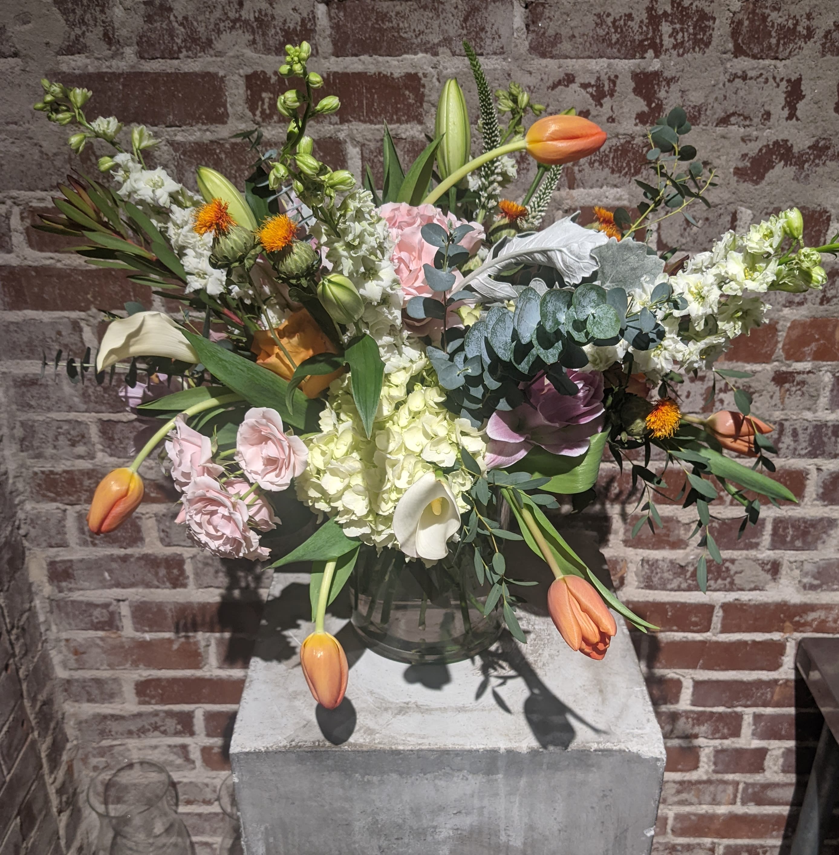 Luxembourg - Classic blend of pastels and whites accented with a variety of textures and foliages. Presented in a clear container with exposed stems.