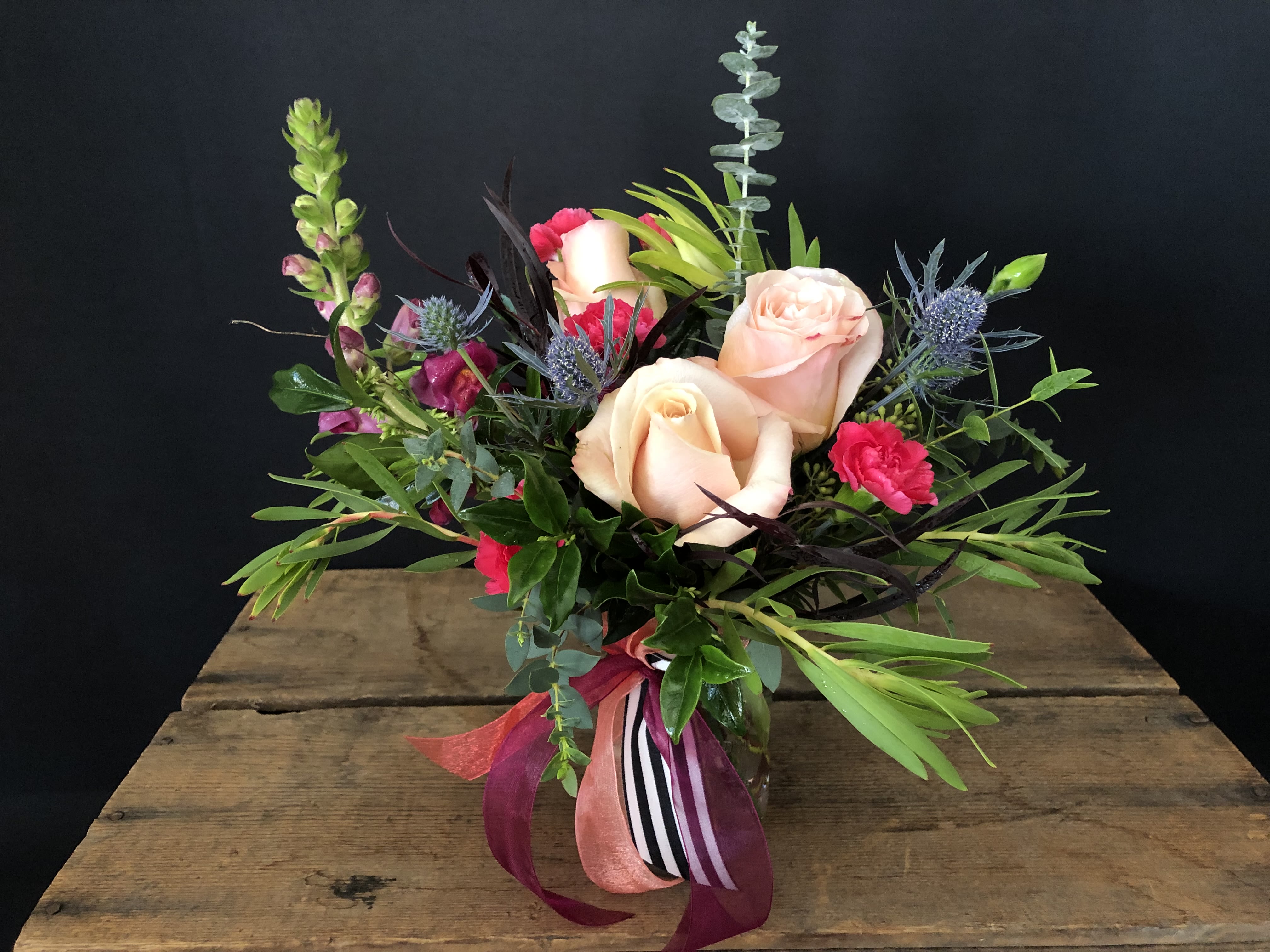 Petite Charm -  The Petite Charm Arrangement  Sweet, stylish, and oh-so-charming—this little design is proof that the best things come in small packages. Tucked into a mason jar with a playful striped ribbon, it’s the perfect pop of beauty for a desk, bedside, or cozy corner. With its mix of seasonal blooms and fresh greenery, this arrangement is brimming with personality and everyday joy. Compact, cute, and completely irresistible—it’s no wonder we’re obsessed with this little cutie. 