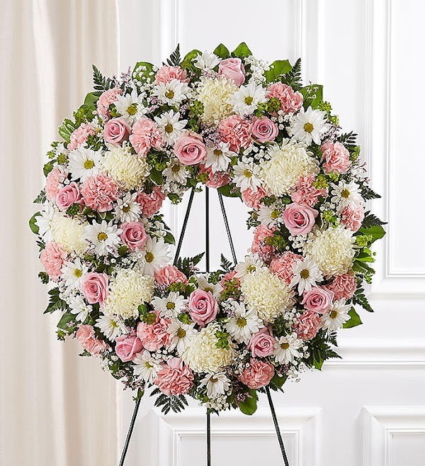Large pink and white floral wreath of roses, carnations, daisies, and mums on a metal easel