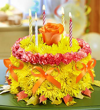 Birthday Flower Cake for Fall - Product ID: 91903  EXCLUSIVE Surprise! Weâve given our signature birthday cake arrangement a sweet new look for Fall. This bright mix of poms and mini carnations, topped with a single Autumn rose and accented with dried oak leaves and a satin ribbon, is a truly original way to serve up smiles on their special day. Fresh, hand-crafted cake-shaped arrangement of mini carnations and cushion poms in floral foam, topped with a single rose Features accents of dried oak leaves and a satin ribbon Arrives in a bakery box with a set of candles where available Arrangement measures approximately 6.5"H x 8.5"L Our florists select the freshest flowers available, so colors, varieties and container may vary