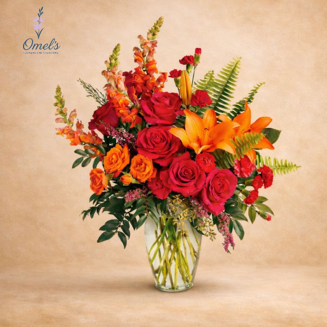 Warm Embrace Tribute - A heartfelt sympathy arrangement designed to express love, comfort, and support. Featuring red and orange roses, vibrant lilies, snapdragons, and lush greenery in a clear glass vase, this design brings warmth and elegance to any memorial setting. Perfect for sending condolences to the home, funeral service, or family gathering.    