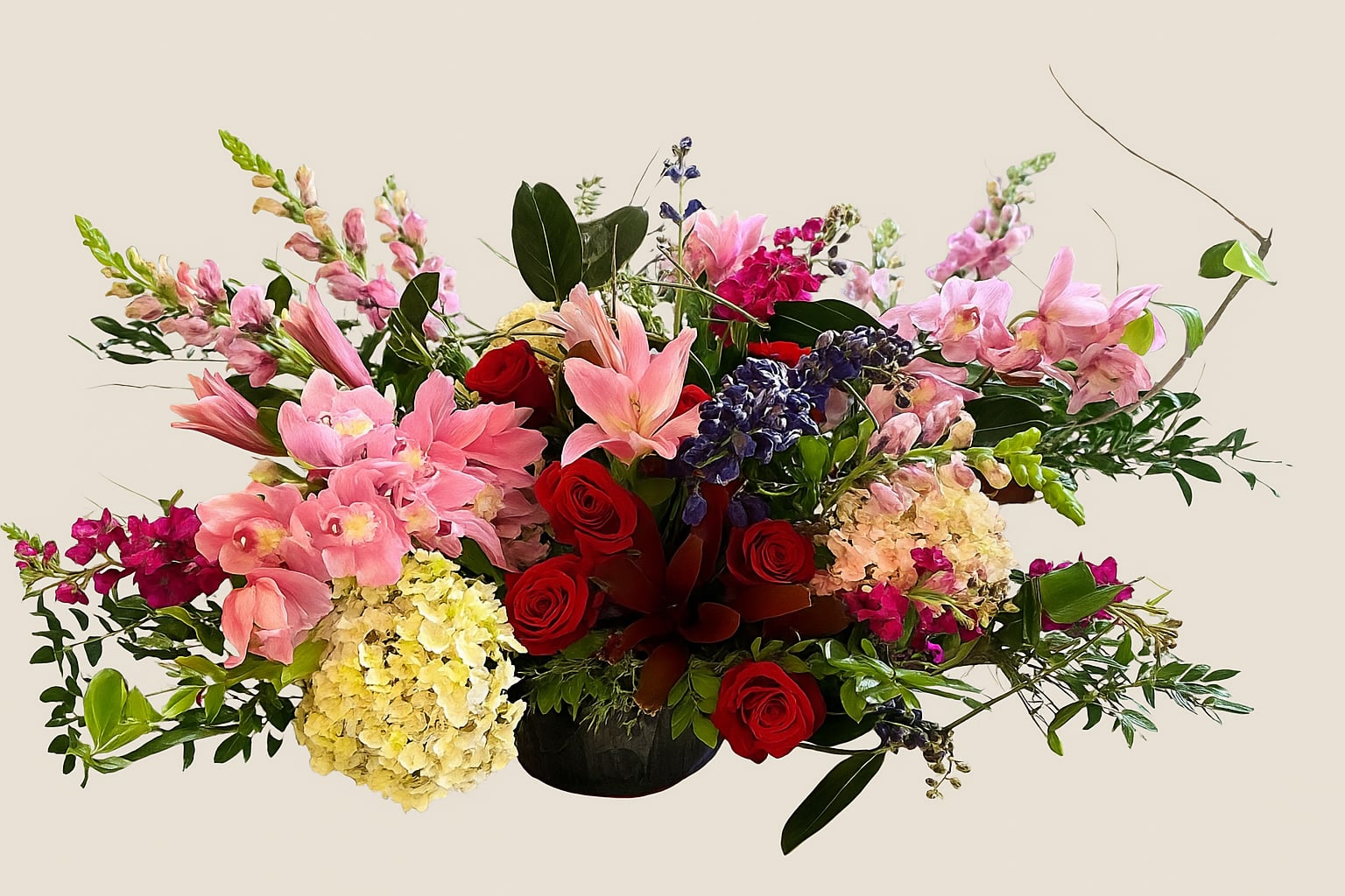 Belgravia Garden Arrangement - A lavish centerpiece of exquisite balance and grace, our Belgravia Garden Arrangement brings the romance of an English garden to the table. Blush cymbidium orchids and soft pink lilies mingle effortlessly with deep red roses, golden hydrangea, and vibrant fuchsia stock, while accents of indigo blooms and cascading greenery lend depth and dimension.  Designed in a low, elegant vessel, this arrangement is perfectly suited for dining tables, sideboards, or intimate gatherings where beauty is best experienced at eye level. Every detail reflects the Savington &amp; Hill heritage of refined floristry—crafted for those who value elegance in its most gracious form.