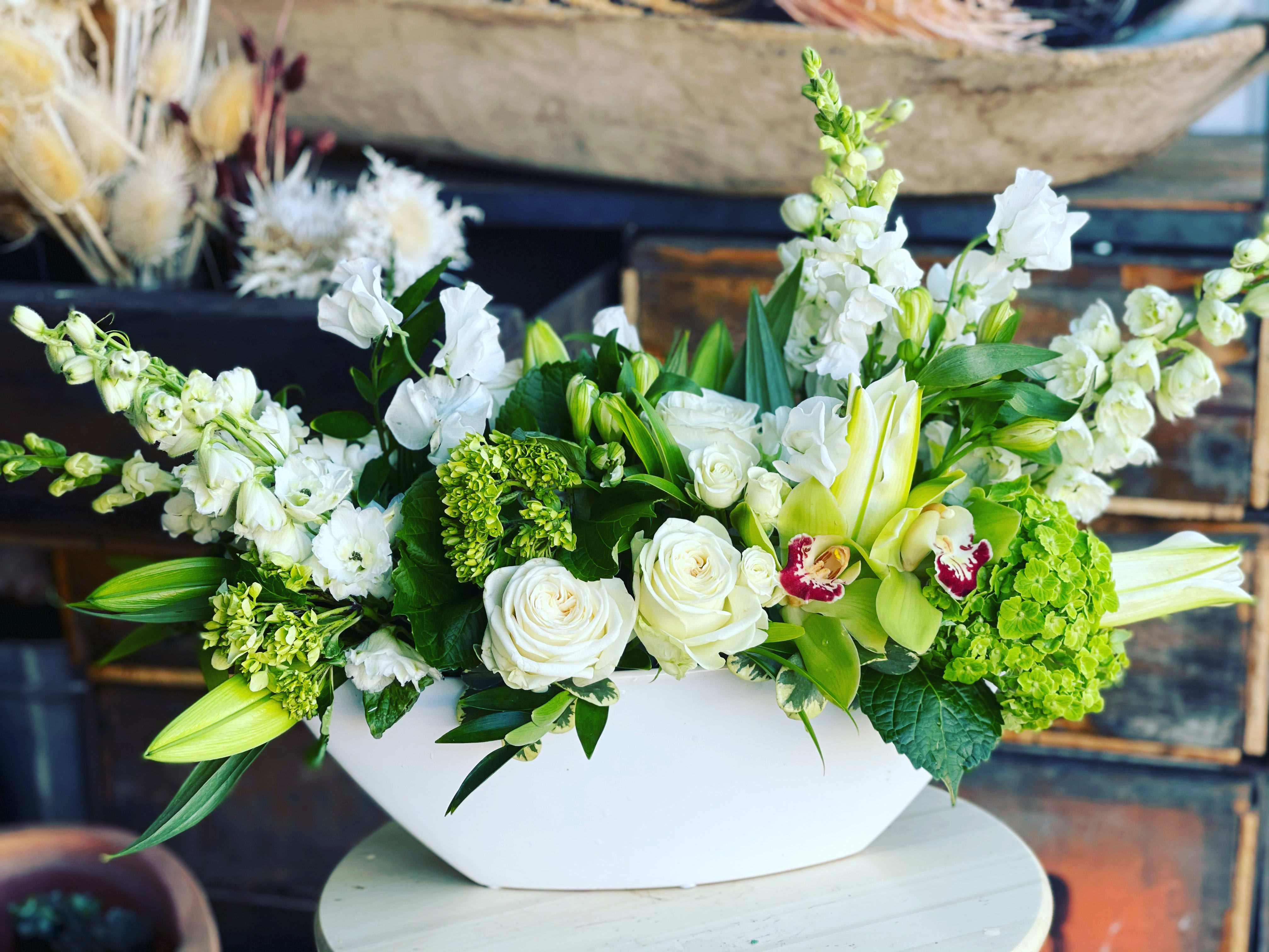 Boat Full Of Blooms - White 12" oval boat shaped vase filled with a bounty of green and white blooms!   We will use the most beautiful, seasonal blooms for this gorgeous piece.  Hydrangea and orchids are a must.  A gorgeous piece for all occasions.  