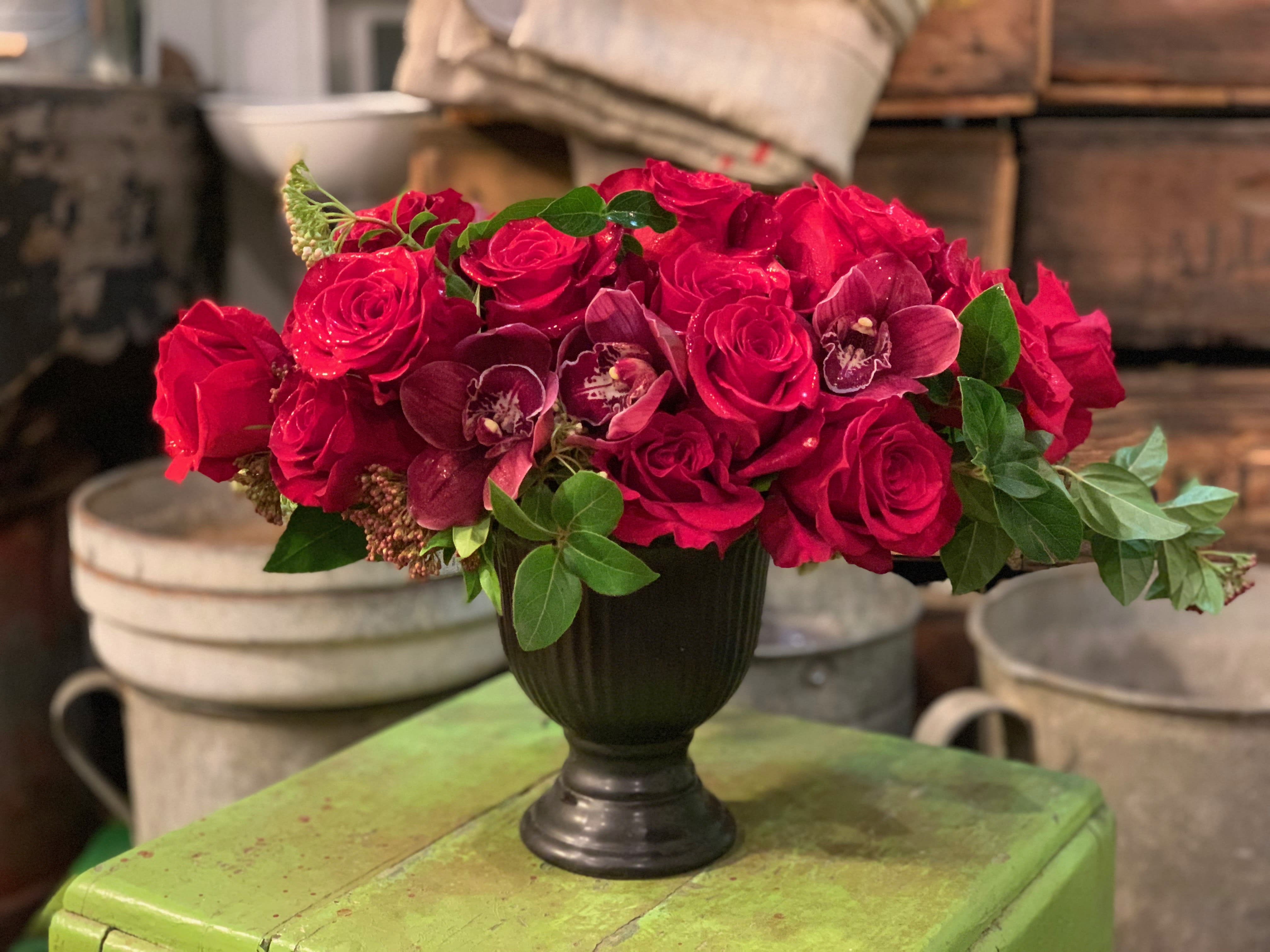 Crazy Love - One dozen red roses and red orchids get together to make this crazy love ensemble displayed in a black pedestal vessel for a more dramatic effect. Black pedestal vessel is sold out. Comparable black vessel will be used 
