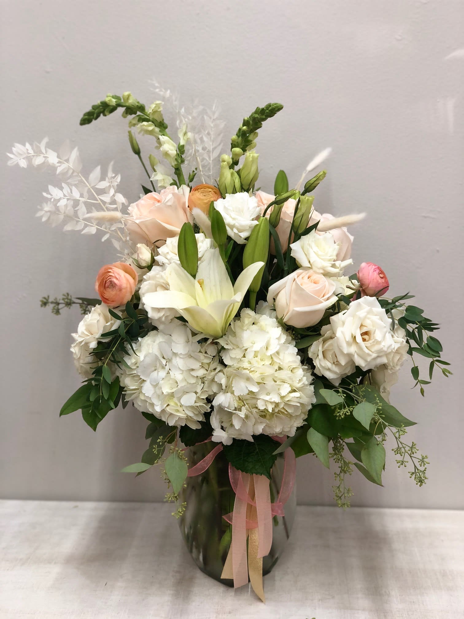 Juliet Bouquet - Hydrangeas, roses, spray roses, ranunculus, lisianthus, snapdragons, bunny tails, preserved ruscus, and assorted greenery arranged in a clear vase.  Flowers AND colors may vary depending on availability. 