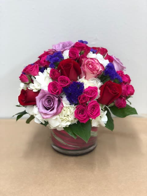 Melting My Heart Bouquet - Lavender, pink and red roses, with hot pink spray roses and a touch of purple statice engulfed in white hydrangeas and a touch of greenery.   Flowers and colors may vary depending on availability.
