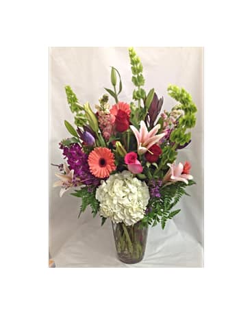 Untamed Beauty Bouquet - In this hand arranged bouquet you see white Hydrangea, pink/red Roses, pink Lilies, coral Gerber Daisies, purple Stock, pink Snap Dragons, Bells Of Of Ireland and Wax Flower.   Flowers and Colors are subject to change due to availability.    FCF-0220