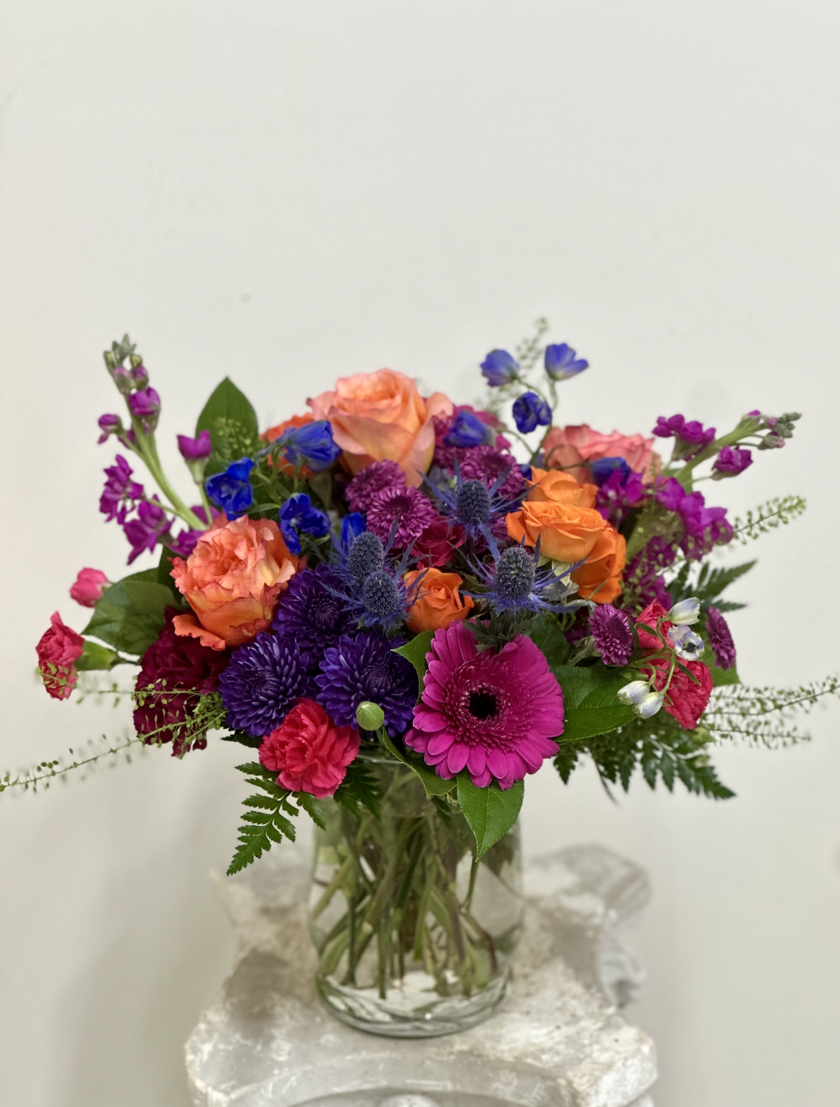 Floral Rhapsody by Westford Florist Art by Veny - Elevate your space with the exquisite Floral Rhapsody by Westford Florist Art, crafted by the talented Veny. This stunning arrangement features a harmonious blend of vibrant gerberas, elegant roses, delicate spray roses, cheerful dot poms, and charming carnations—all artfully accented by thistle and delphinium atop a lush bed of greenery. Perfect for any occasion or as a standout centerpiece in your home or office, Floral Rhapsody captures the beauty of nature while exuding sophistication. Each bloom is thoughtfully selected to ensure lasting freshness and delight. Experience the artistry of floral design with this captivating piece that brings warmth and joy to any environment. Perfectly curated for those who appreciate elegance in every detail.