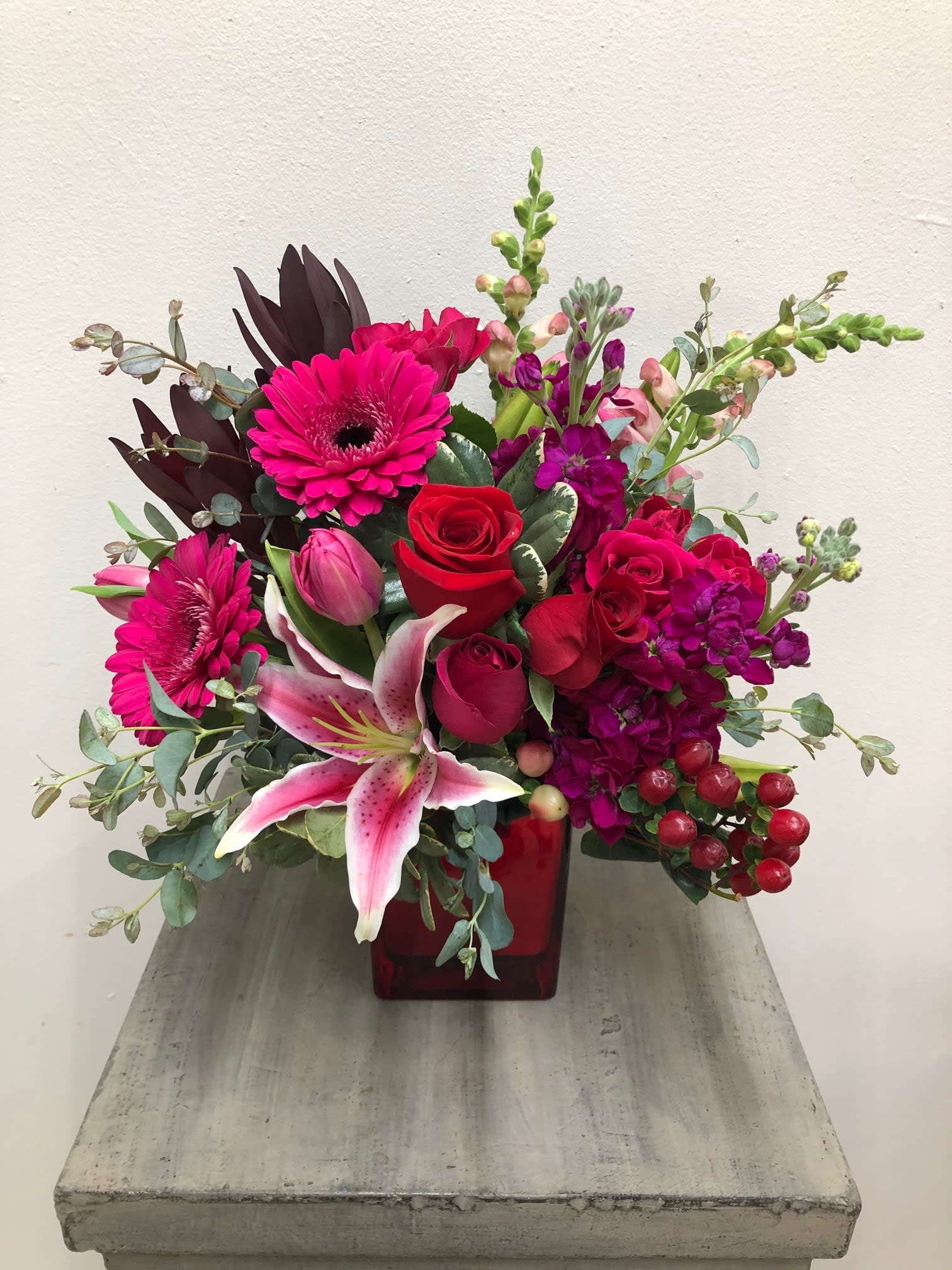 Rouge Bouquet - Short red cube with deep colors such as hot pink, magenta and red. Mixed flowers such as roses, gerbers, lilies, snaps, stock, tulips, and more...  CONTAINER SOLD OUT/ WILL BE SUBSTITUTED FOR CLEAR CUBE Flowers and colors may be substituted depending on availability. 
