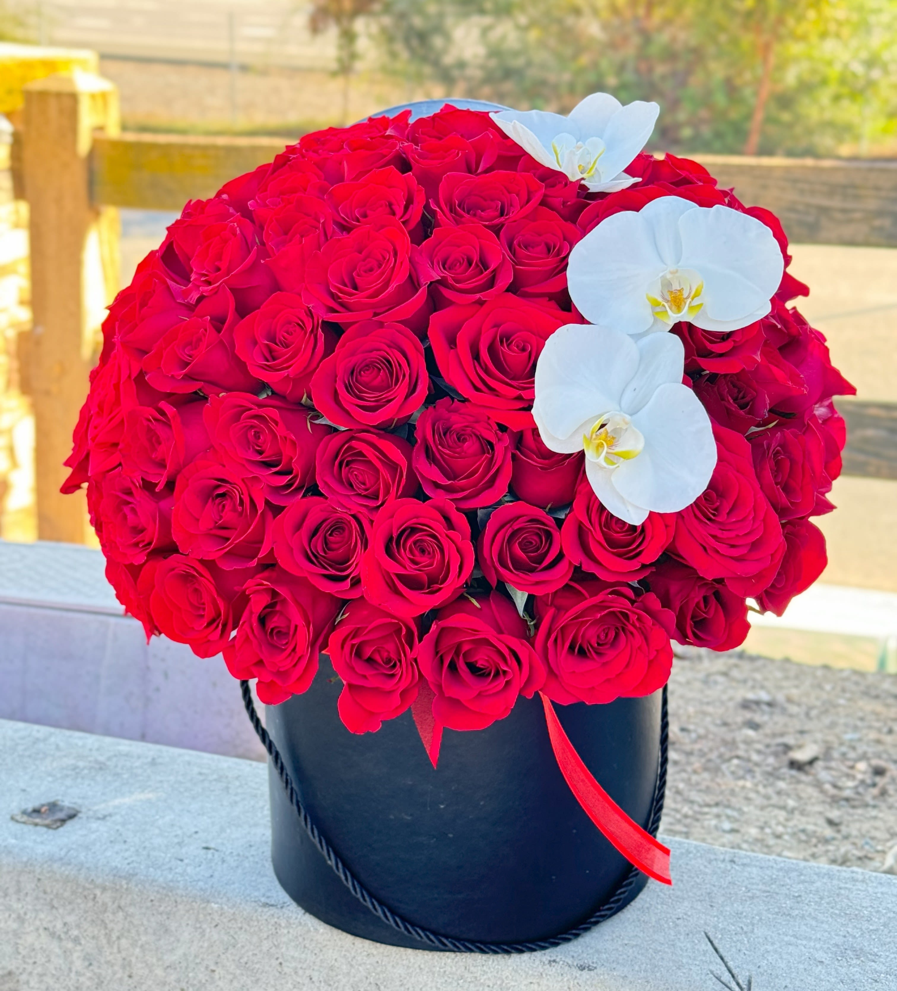 Scarlet Symphony- Flowers in a Box - Make a grand impression with this luxurious arrangement of over 50 velvety red roses accented by elegant white phalaenopsis orchids, all presented in a sleek black hat box. A timeless symbol of love and passion, this bouquet is ideal for Valentine’s Day, anniversaries, or a luxury romantic gift.  Crafted by expert florists at Hollywood Blooms, this premium flower box is available for same-day delivery in Los Angeles. Surprise your loved one with a bold and unforgettable floral statement.  Order online today and experience world-class floral design.