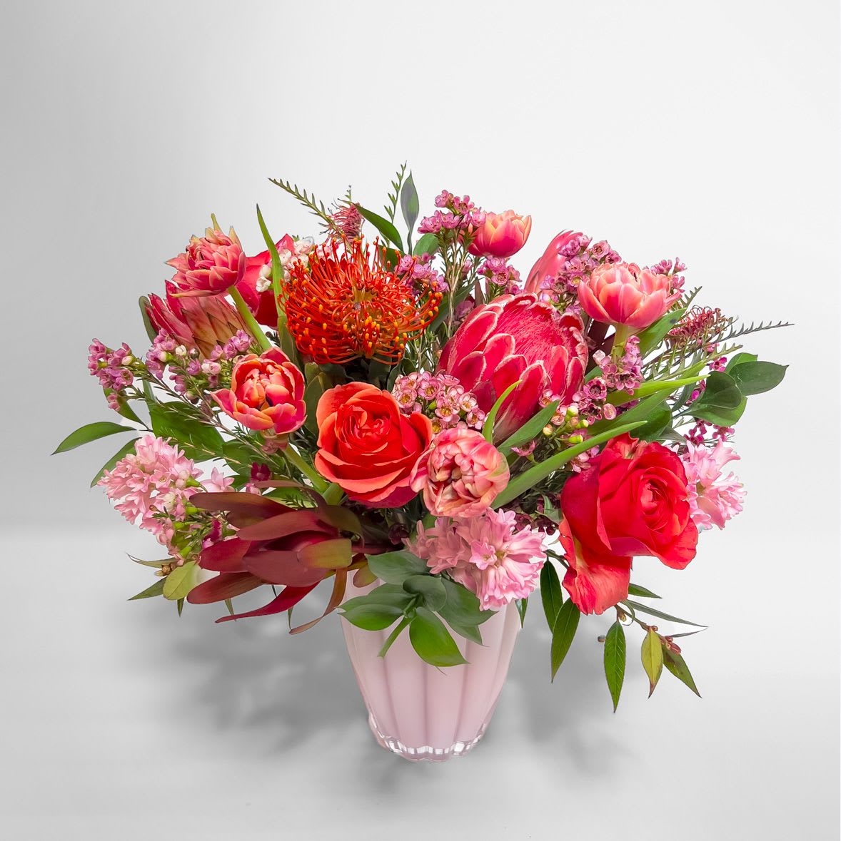 Dawn - This stunning pink arrangement features a blend of lush coral roses and exotic protea. This design strikes the perfect balance between elegance and wild beauty. 