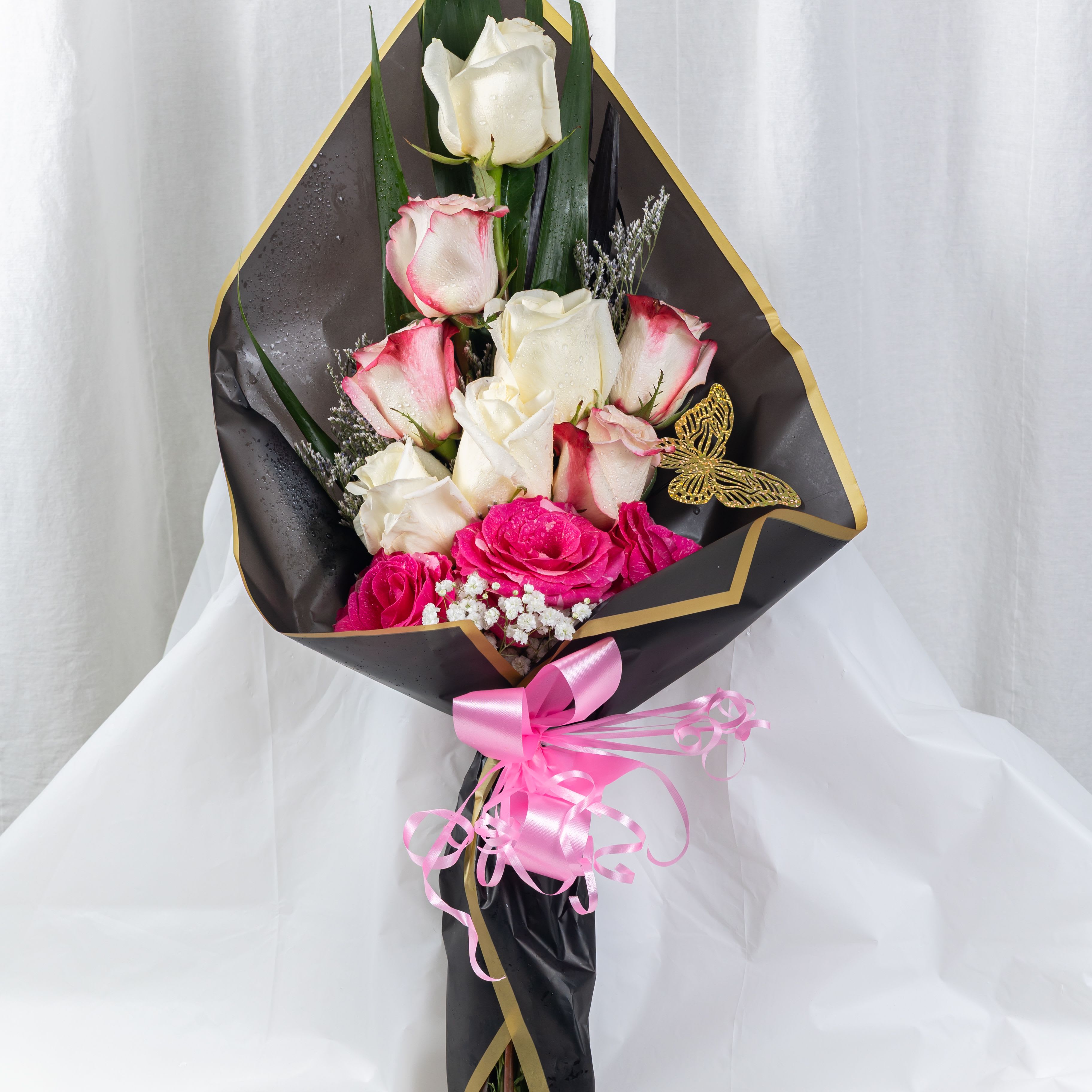 Gilded Romance - A luxurious bouquet of pink-edged white roses and vibrant pink blooms, wrapped in black and gold paper with a satin ribbon and golden butterfly accent. This elegant arrangement blends celebration and charm—perfect for birthdays, anniversaries, or heartfelt surprises.