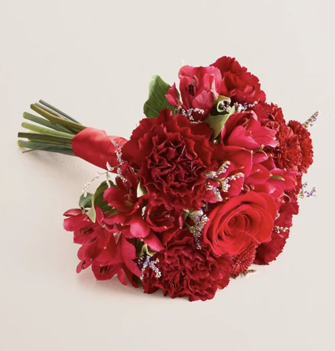 Red Prom Handheld Bouquet  - Standard: bouquet features a red rose; red Peruvian lilies (alstroemerias) and button poms;  burgundy carnations; and a purple limonium with a hand-tied red ribbon; measures 6”H x 6”W  Deluxe: bouquet features red roses, Peruvian lilies (alstroemerias), mini Gerbera daisies, and button poms;  burgundy carnations; and a purple limonium with a hand-tied red ribbon; measures 7”H x 7”W