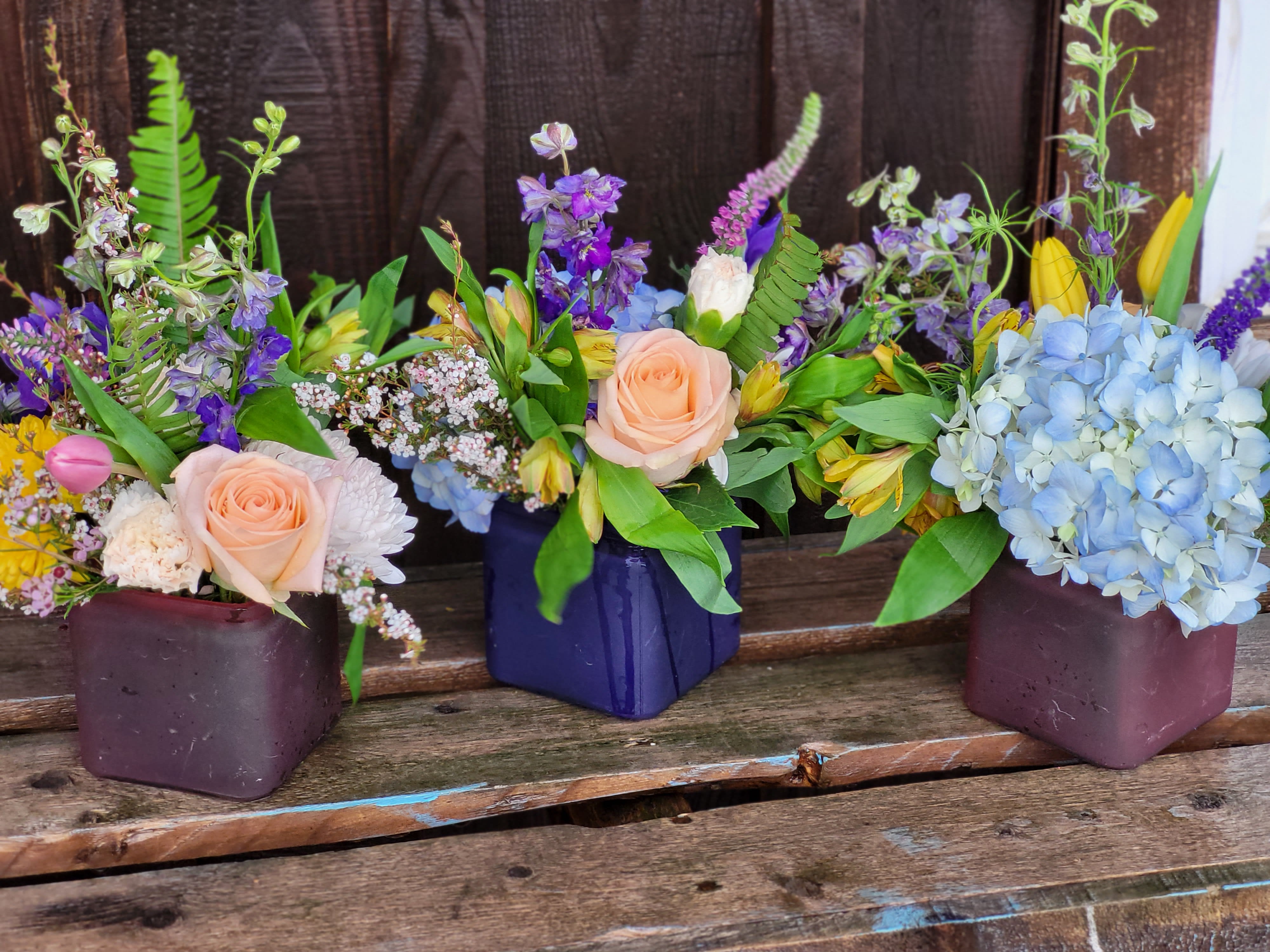 Spring Colors Designers Choice Cube Vase - A soft colorful spring mix of flowers in a assorted colored cube vases. These low, yet lush bouquets are great as a simple centerpiece, or desktop florals! Various colors available.