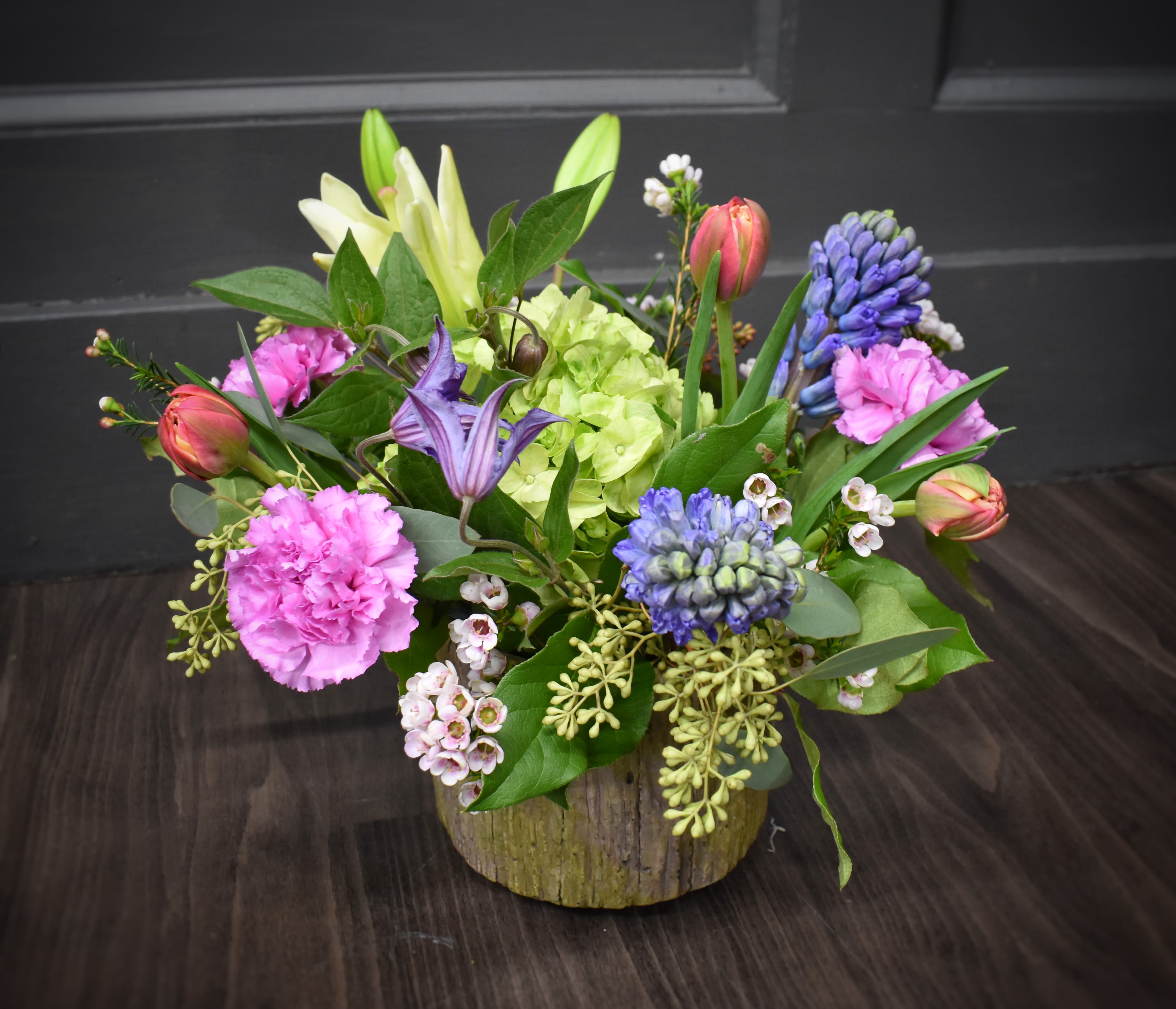 Garden Gathering - An embossed ceramic container filled with cream and shades of purple flowers. Fragrant hyacinth, lily, hydrangea and tulips fill out this beautiful floral gift. appx 12"h x 10"w