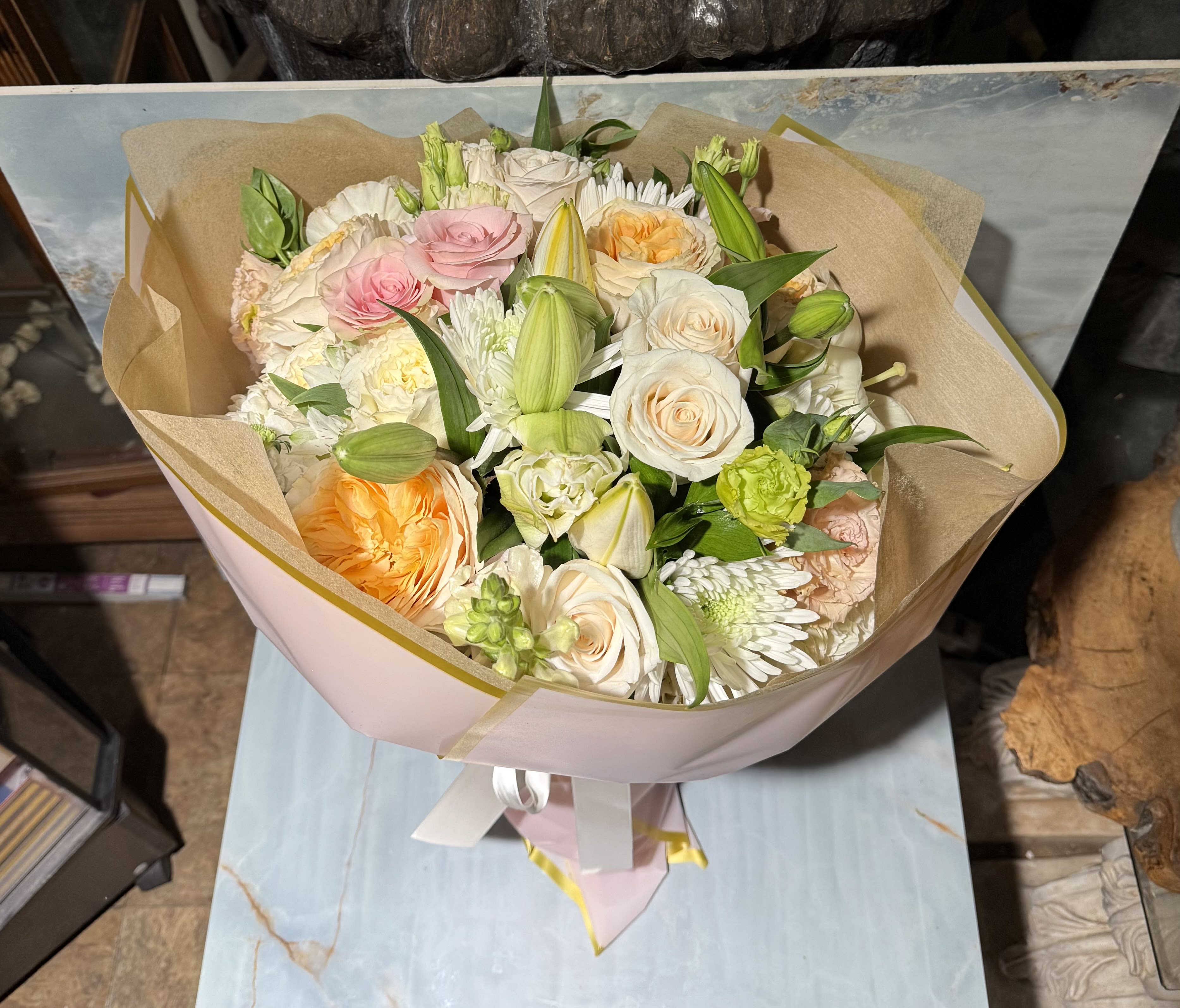 Blushing Harmony  - This bouquet feels soft, elegant, and beautifully balanced-full of gentle color and fresh texture. Creamy ivory and blush roses mingle with warm peach garden roses, while delicate white chrysanthemums and fresh green lily buds add depth and movement. Touches of pale green blooms and lush foliage keep the arrangement feeling airy and natural. 