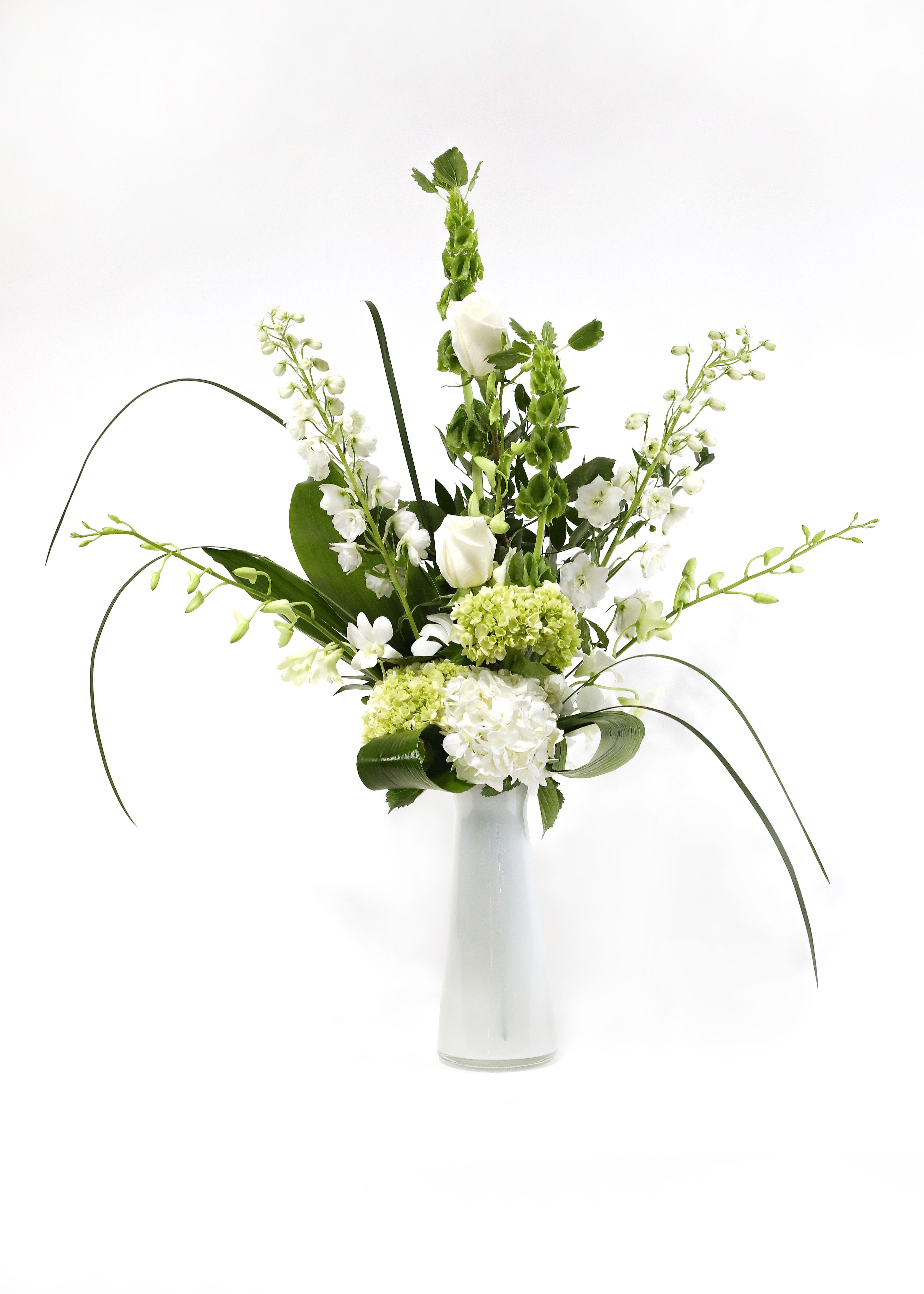 NEW BEGINNINGS - THIS SIMPLE ELEGANT ARRANGEMENT EASES TENSION JUST FROM ITS PHOTOGRAPH. IT HAS ORCHIDS, WHITE &amp; MINI GREEN HYDRANGEA, BELLS OF IRELAND, WHITE ROSES, AND WHITE DELPHINIUM. PRESENTED IN A TALL WHITE GLASS VASE. 