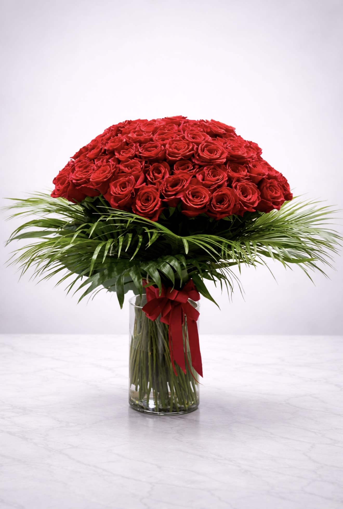 Grand Crimson Majesty  - Make a breathtaking impression with our Grand Crimson Majesty arrangement, featuring 75 premium long-stem red roses beautifully arranged in a full dome design. Styled with elegant tropical greenery and presented in a modern clear glass vase with a satin red ribbon, this design embodies romance, luxury, and sophistication.  Perfect for anniversaries, Valentine’s Day, proposals, or milestone celebrations, this stunning red rose bouquet is handcrafted by AZ Flowers &amp; Gifts and available for same-day flower delivery in Alpharetta, GA 30022 and surrounding areas.  Order luxury red roses in Alpharetta today and surprise someone with an unforgettable floral statement.