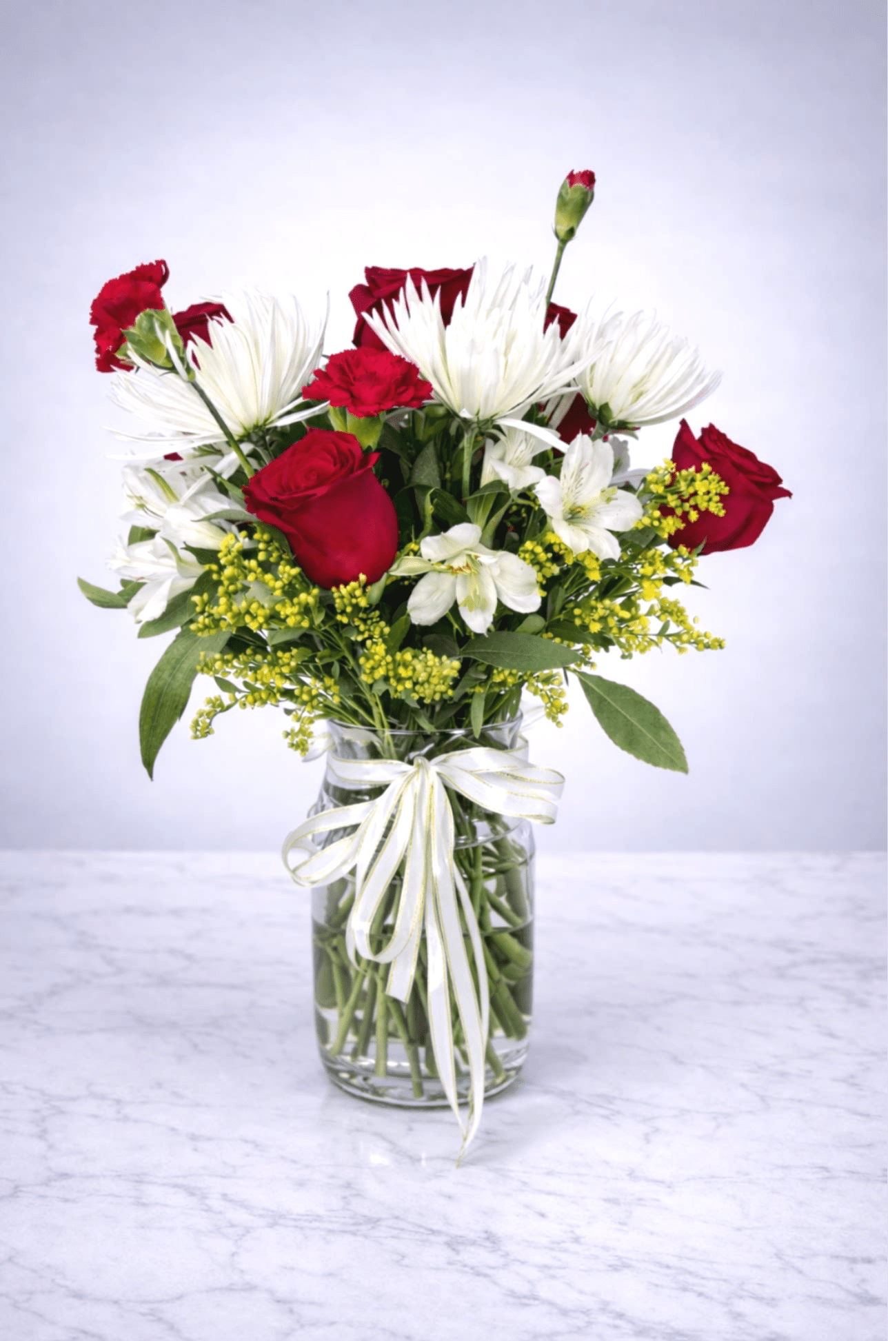 Crimson Snow Elegance - A striking mix of red roses, white spider mums, carnations, and delicate white blooms accented with fresh greenery in a clear vase with a gold-trim ribbon. Bold, romantic, and perfect for anniversaries, celebrations, or heartfelt gifts.