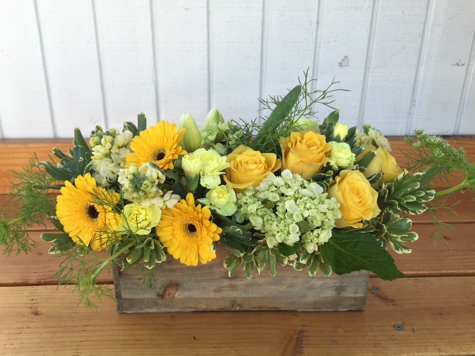 Low yellow flower arrangement with roses and gerbera daisies in a rustic wooden box