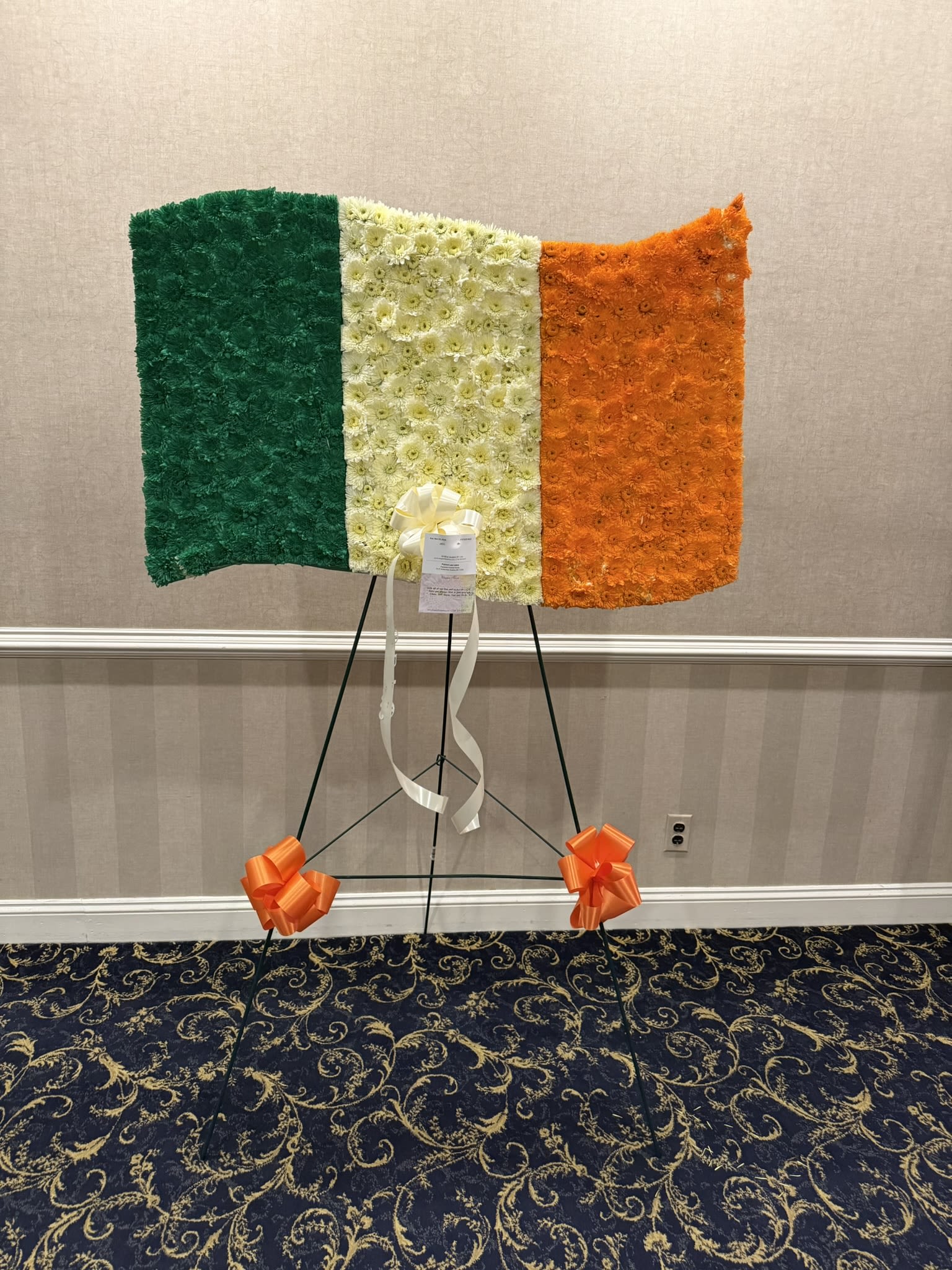 Irish Flag  - This beautiful floral tribute captures the spirit of **Ireland** in full bloom  Rising proudly in vibrant green, pure white, and bold orange, the arrangement reflects the heart and history of the Irish nation. The **green** stands for the rich landscapes and enduring Gaelic tradition — the rolling hills, the resilience, and the deep cultural roots of the Irish people. The **white** at the center symbolizes peace and hope — a promise of unity between traditions. The **orange** represents the Protestant heritage and the legacy of William of Orange, completing a powerful message of inclusion and reconciliation.  Crafted in flowers, this flag feels especially meaningful — living blooms symbolizing a living nation. It is not just a display of colors, but a declaration of identity, courage, and unity. Together, these three bands tell the story of a people who have endured, united, and carried their pride across generations.  A timeless emblem of strength, heritage, and peace. 