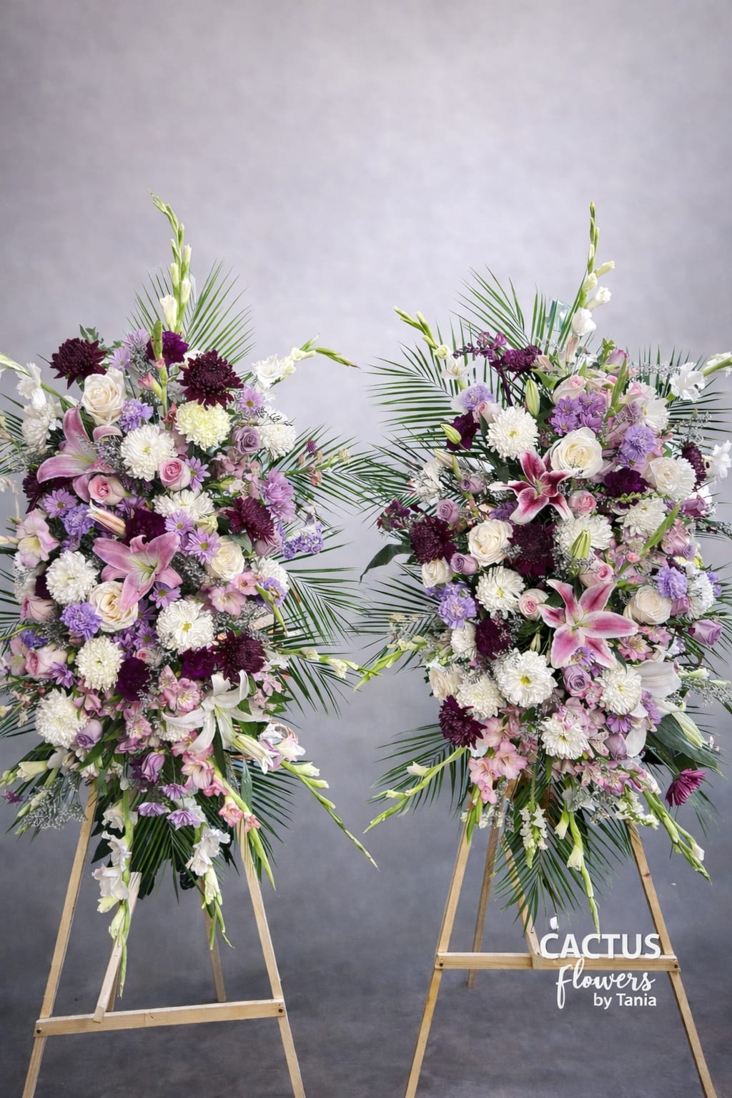 Eternal Harmony – Standing Spray Pair - Two coordinated standing sprays designed to frame the casket beautifully and create a balanced, elegant tribute.  This package includes: • Two full-size standing sprays • Premium mixed fresh flowers • Custom color palette based on family preference • Wooden easels included  Each pair is handcrafted with fresh seasonal blooms such as roses, lilies, mums, snapdragons, gladiolus and specialty accents in your preferred tones.  Designed to be placed on each side of the casket for a symmetrical and impactful presentation.  This design creates a graceful and elevated farewell, offering a cohesive floral presence during services.  Available in soft pastels, all white, bold tones, or custom color combinations upon request. 