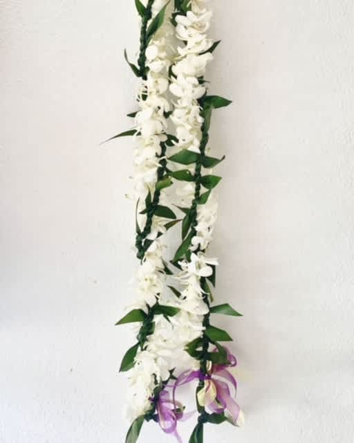 White flower garland with green leaves and a purple ribbon