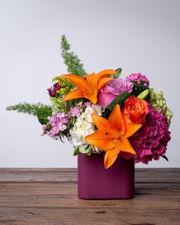 Spice - Add a little Spice. A bright &amp; colorful mix of blooms like lilies, roses &amp; hydrangea in shades of orange, dark pink, lavender, purple &amp; white designed in a burgundy cube.