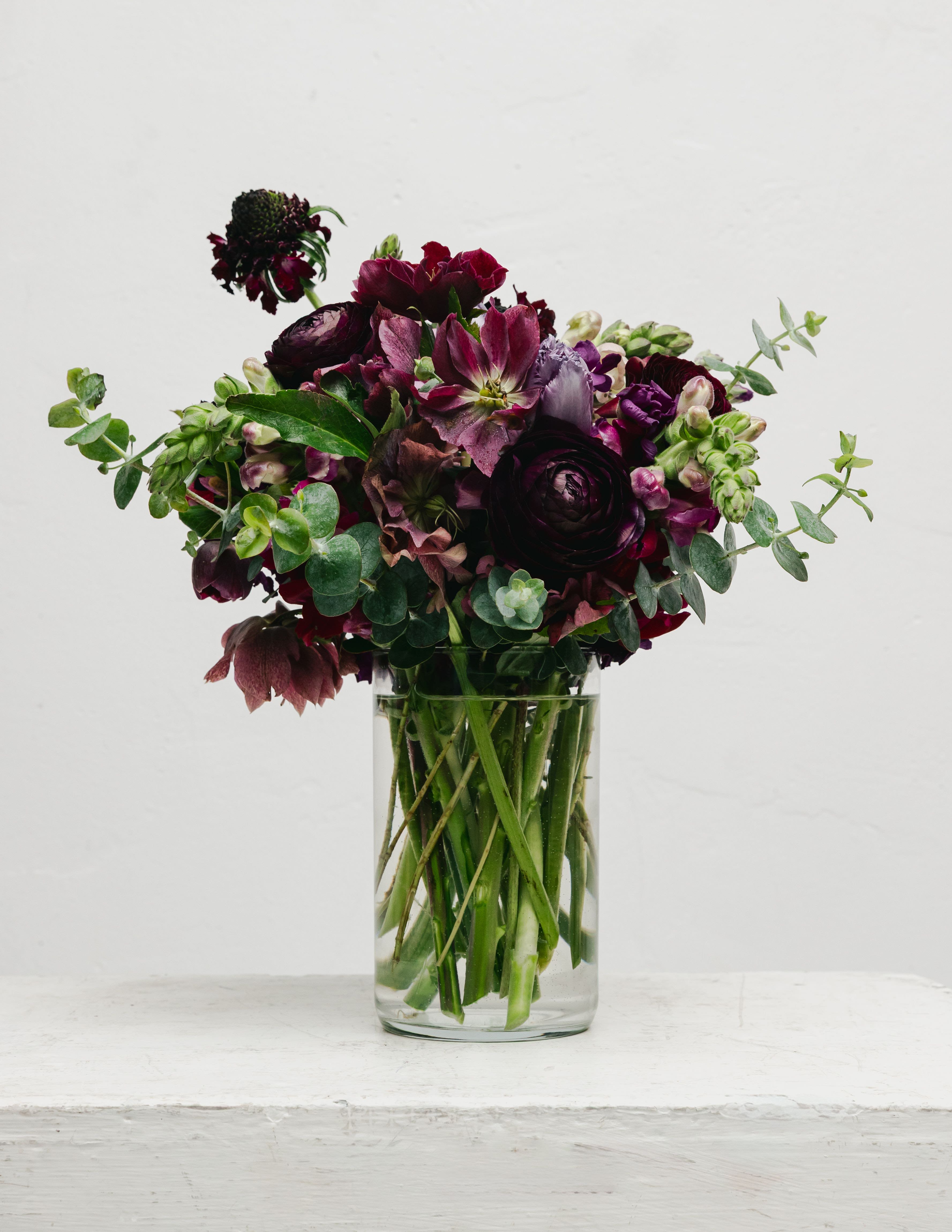 Mini Plum  - The Mini Moody Design is a captivating floral arrangement, perfect for expressing love. Its combination of dark accent blooms, purple anemones, snapdragons, and dusty purple roses creates a beautiful and unique display that resonates with gothic romance.  This arrangement is not just a gift; it's an experience that captures the essence of passion and elegance, making it a memorable surprise for anyone who appreciates a touch of dark beauty.  Vase Size 5 inches   Design might vary from the photo due to flower availability and season, but we will ensure it is fresh and beautiful!