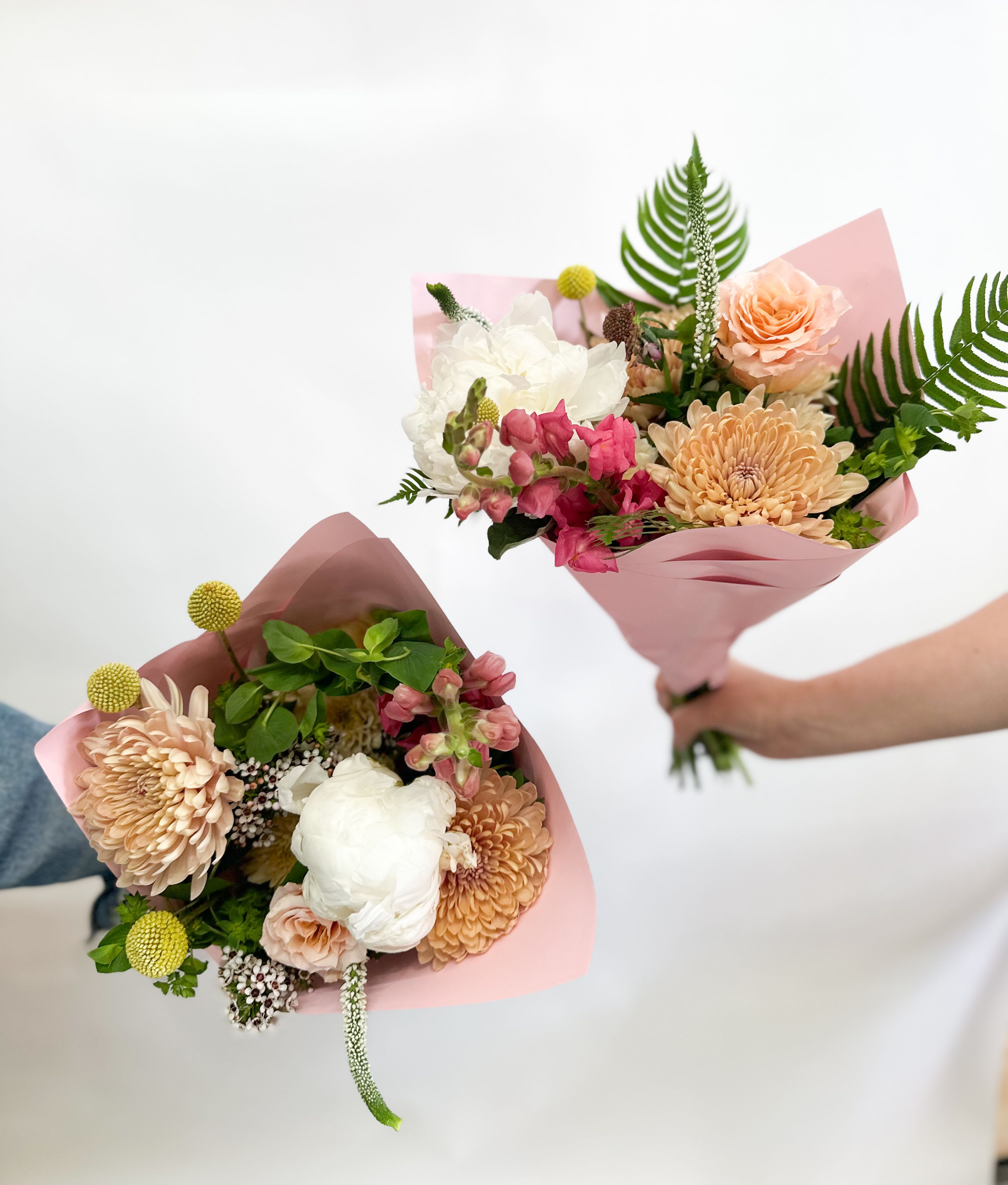 Two hand-held bouquets with peach, white, and pink flowers