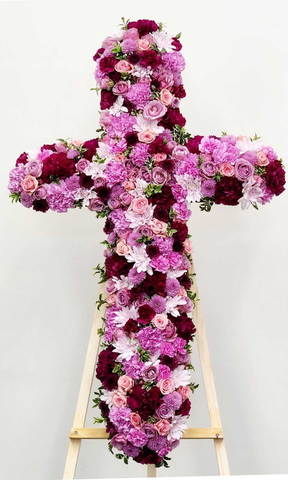 Faithful Cross - The Faithful Cross is a stunning tribute arrangement crafted to honor and celebrate a cherished life. This elegant design features a harmonious blend of burgundy, lavender, and soft pink blooms—including premium roses, spray roses, carnations, and mums—arranged in a lush cross formation. Each flower is thoughtfully selected to create depth and movement, offering both beauty and comfort during meaningful moments. Perfect for services, memorials, or as a heartfelt gesture of sympathy and remembrance.