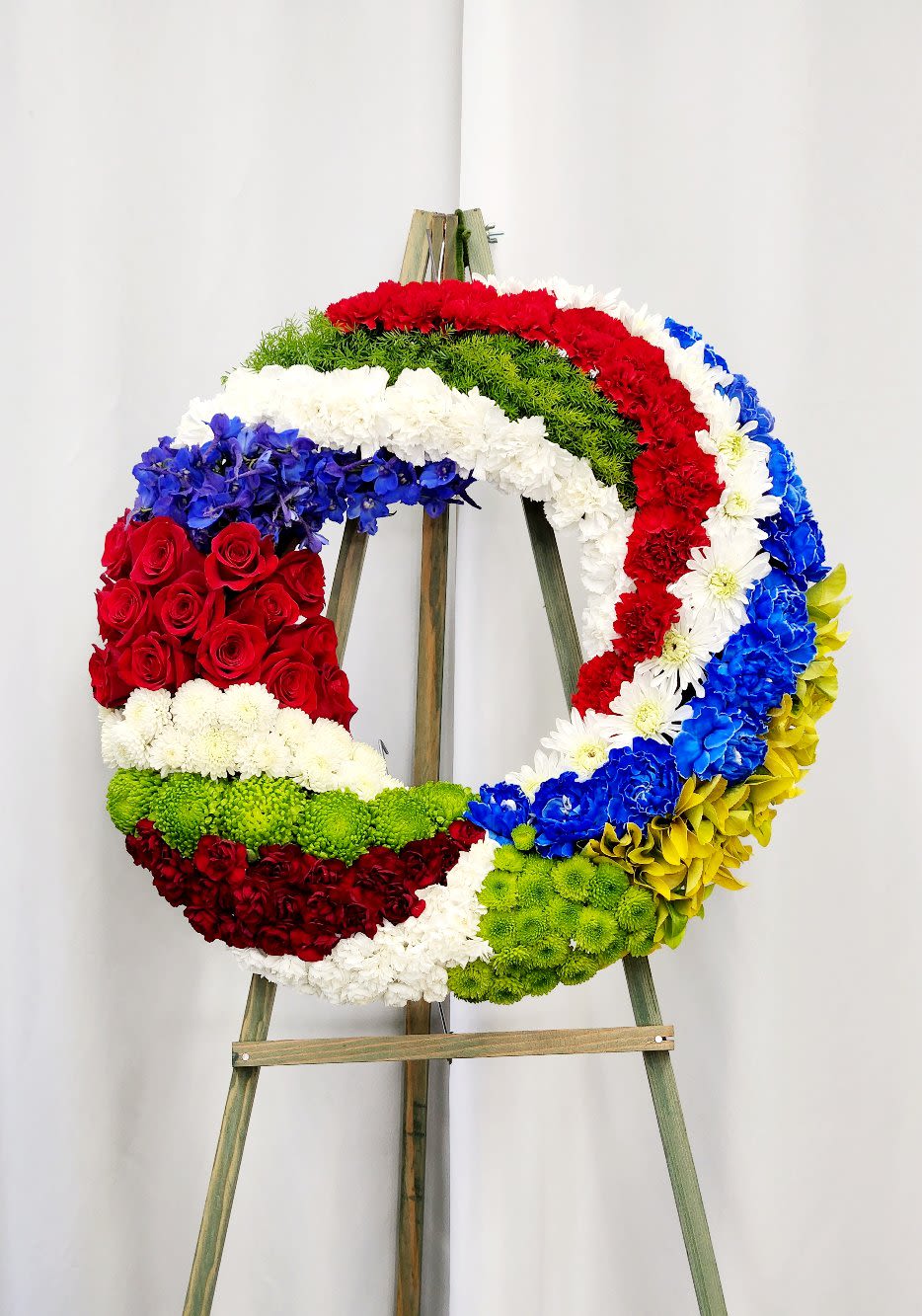 Spiral Red, White and Blue Wreath - Celebrate patriotic pride with this stunning 30" spiral wreath, a showstopping design that commands attention in any space. Vibrant red, white, and blue blooms dance in a graceful spiral pattern, creating dynamic movement and visual interest. Perfect for Independence Day, memorial occasions, or year-round patriotic display, this generous-sized wreath brings timeless beauty and heartfelt sentiment to your home or venue. ONE SIZE ONLY AS PICTURED: PREMIUM 30"