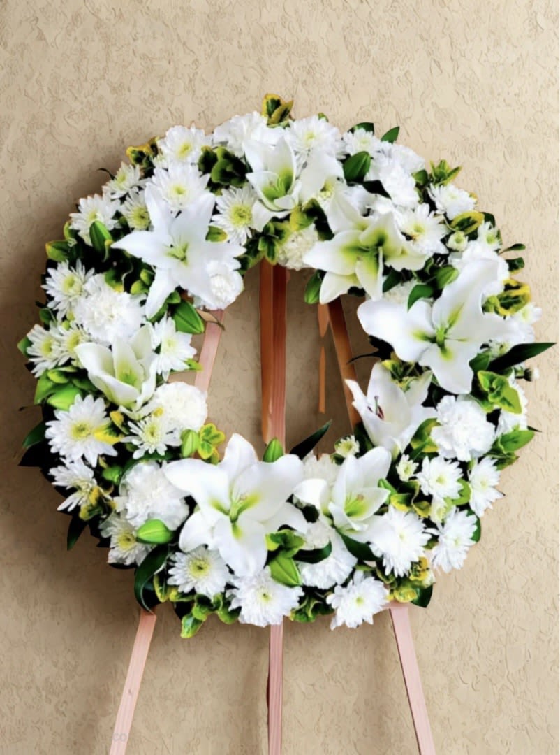 Loving Farewell Wreath - Celebrate a life with grace and dignity through this sophisticated memorial wreath. Crafted with pristine white roses, chrysanthemums, and lilies, each bloom is thoughtfully arranged to convey compassion and respect. The all-white palette creates a timeless, elegant tribute that honors cherished memories while offering solace during difficult moments. Perfect for services, viewings, or as a heartfelt gesture of sympathy.