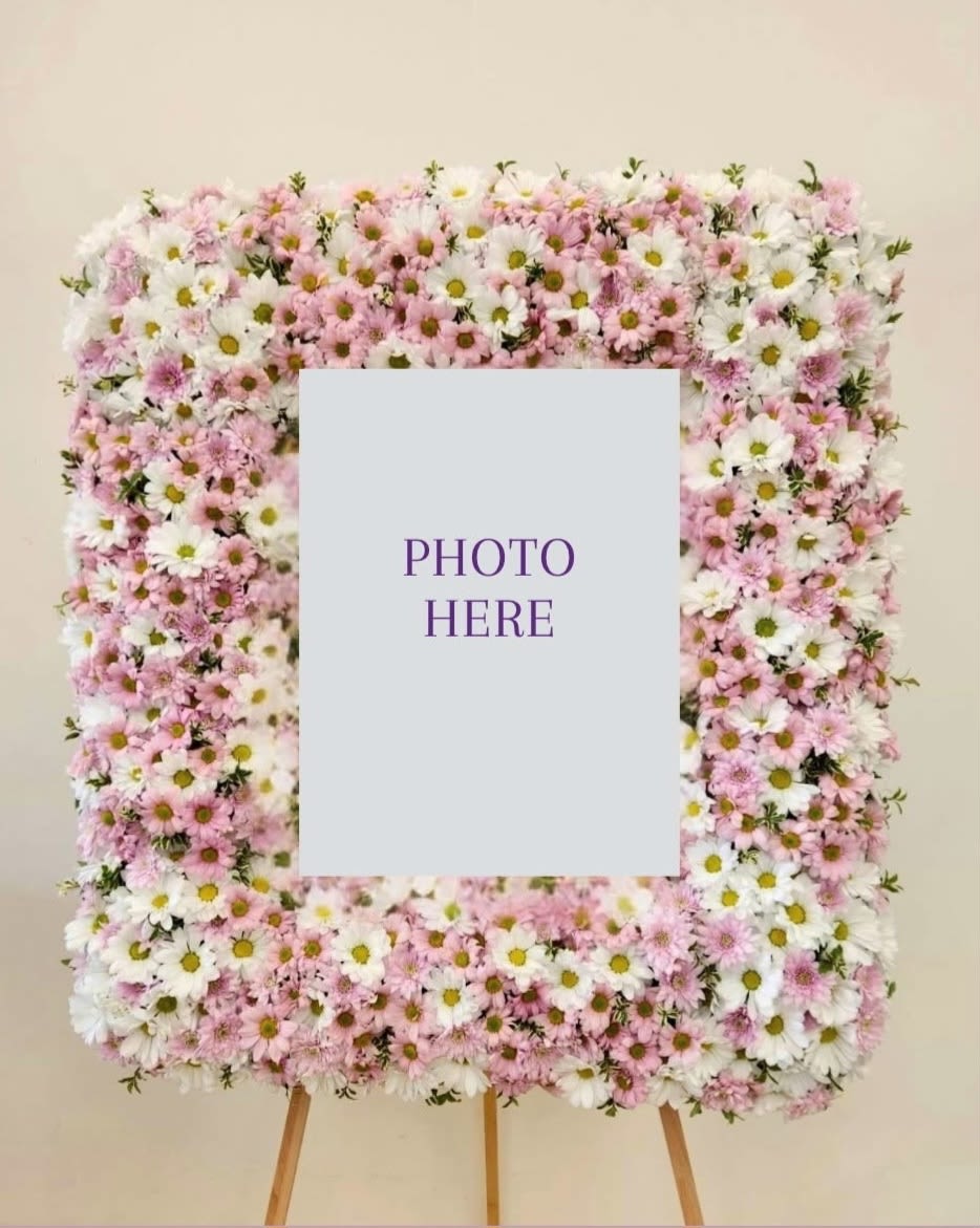 Custom Photo Frame Daisies Pink and White - A timeless tribute crafted with fresh blooms arranged around a cherished photograph. This custom floral frame transforms a beloved image into a living memorial, perfect for displaying at services, celebrations of life, or intimate gatherings. Each arrangement is thoughtfully designed to honor your loved one with natural beauty and elegance. An meaningful way to keep their memory present and celebrated. ONE SIZE ONLY.  PICTURE SIZE: 24" Tall by 22" Wide  Finished Photo Frame 36" Tall by 30" Wide  FOR SPECIFIC FLOWERS AND COLORS, PLEASE CONTACT THE SHOP AT 562-426-6996  OR VISIT OUR LOCATION AT 611 EAST CARSON STREET, SUITE B, LONG BEACH, CA, 90807