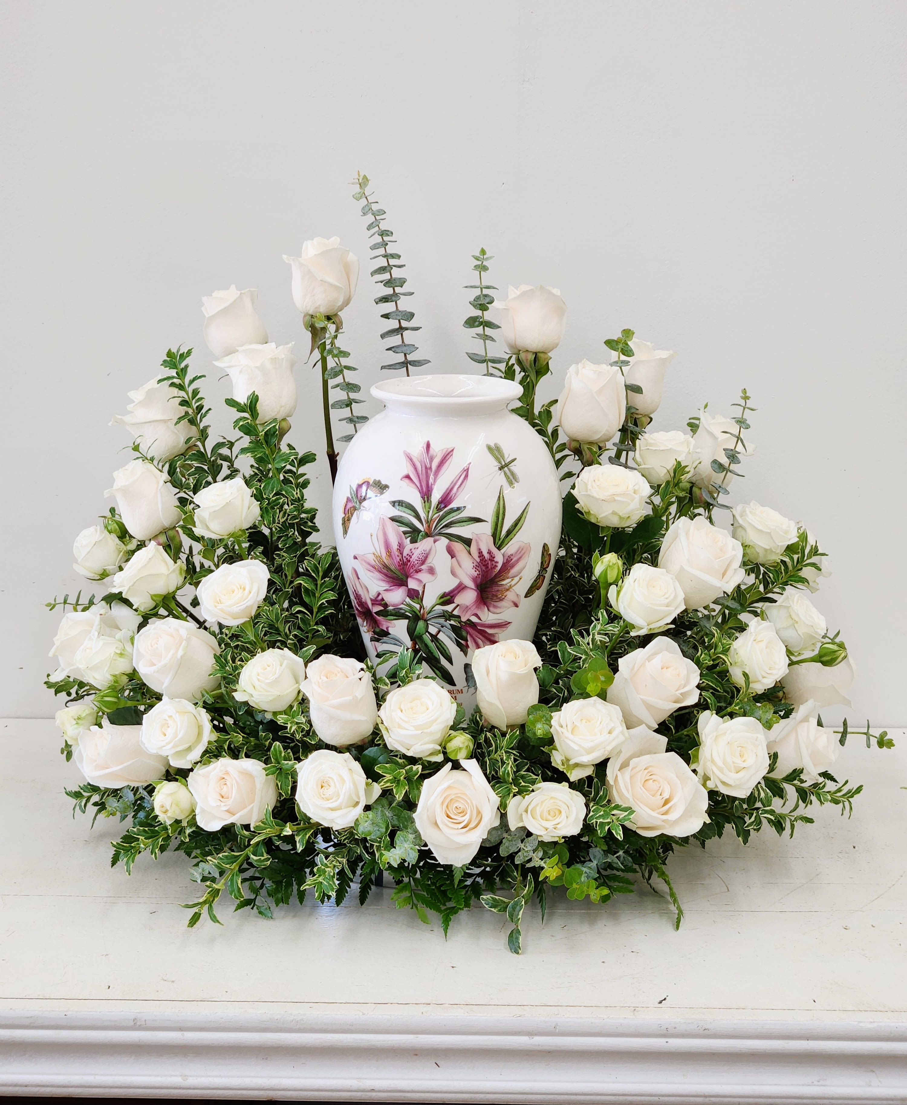 Sweet Remembrance - Sweet Remembrance honors your loved one with timeless elegance. This all-white cremation arrangement features full, lush roses cradling the urn, softened by gentle green foliage in a graceful rounded form. A serene tribute that speaks to enduring love and cherished memories.  Approximate Size:  Standard: 18 Roses, 18" Wide by 12" Tall  Deluxe: 24 Roses, 20" wide by 14" Tall  AS PICTURED: PREMIUM SIZE: 36 Premium Roses. 22" Wide by 20" Tall