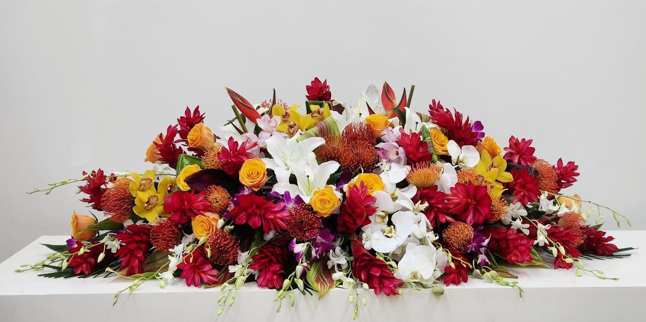 Tropical Memory - A luxurious and one-of-a-kind tropical casket spray, bursting with vibrant color and elegance. Featuring a stunning blend of exotic blooms in rich, tropical hues — from brilliant orchids and bold anthuriums to lush greenery — this design celebrates life with warmth, beauty, and island-inspired grace. A radiant tribute as unique as the life it honors.  AS PICTURED: PREMIUM 50"L by 34"D