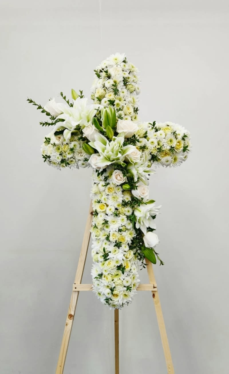 Love and Devotion Cross - Love and Devotion Cross features an elegant arrangement of white blooms—roses, mums, and button flowers—accented with touches of soft green with cascading blooms of lilies across the face. This serene design embodies pure elegance and timeless grace, making it a meaningful tribute for any occasion. Perfect for expressing sympathy, faith, or heartfelt devotion.  AS PICTURED: PREMIUM 36"