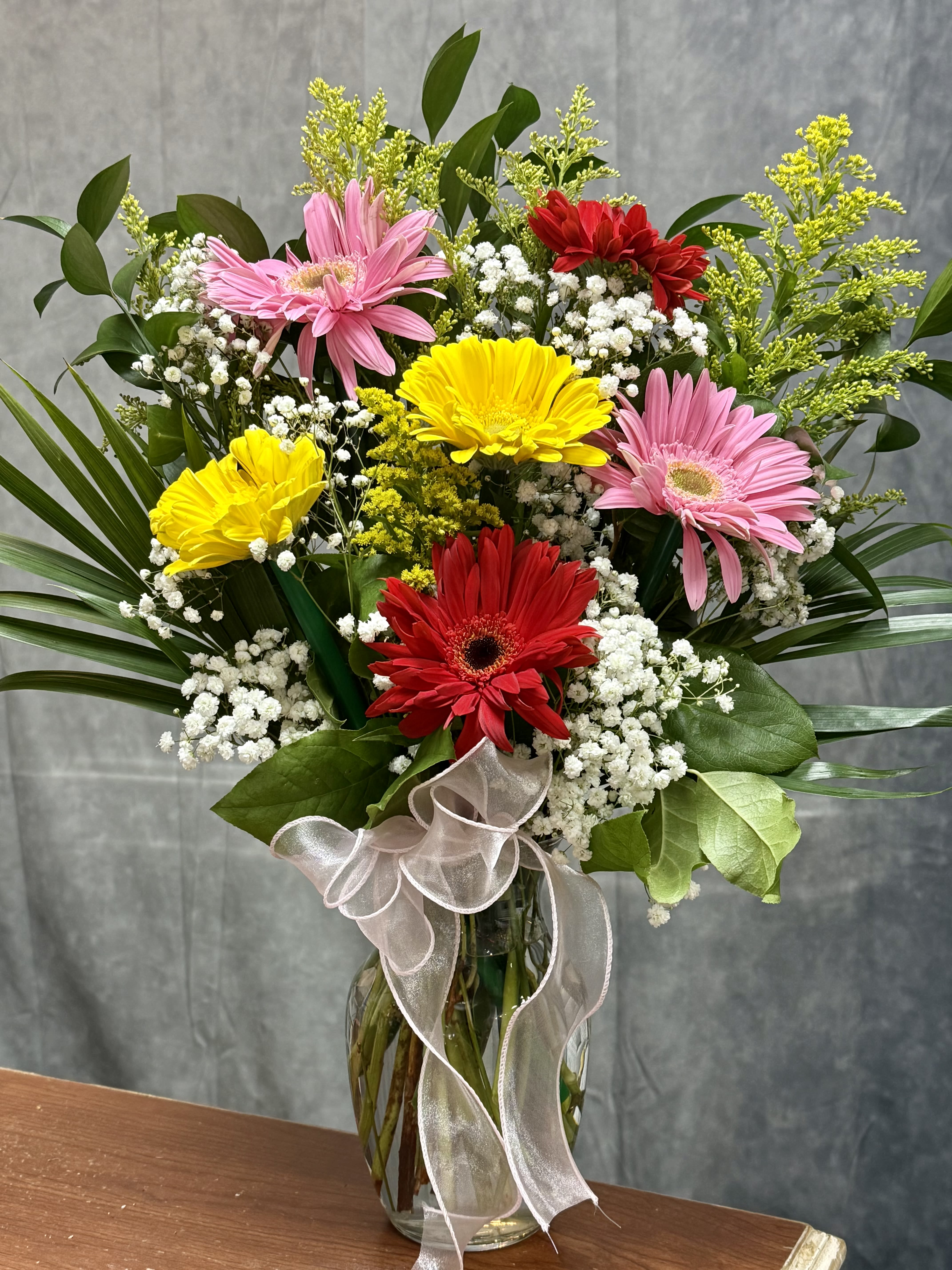 Gerbera Daisies Lovers Vase  - A cheerful mix of vibrant gerbera daisies, accented with baby’s breath, solidago, and fresh greenery. Designed in a clear glass vase and finished with a soft ribbon, this bright arrangement is perfect for birthdays, get well, thank you, or just because.  Handcrafted with love at J&amp;S Floral 