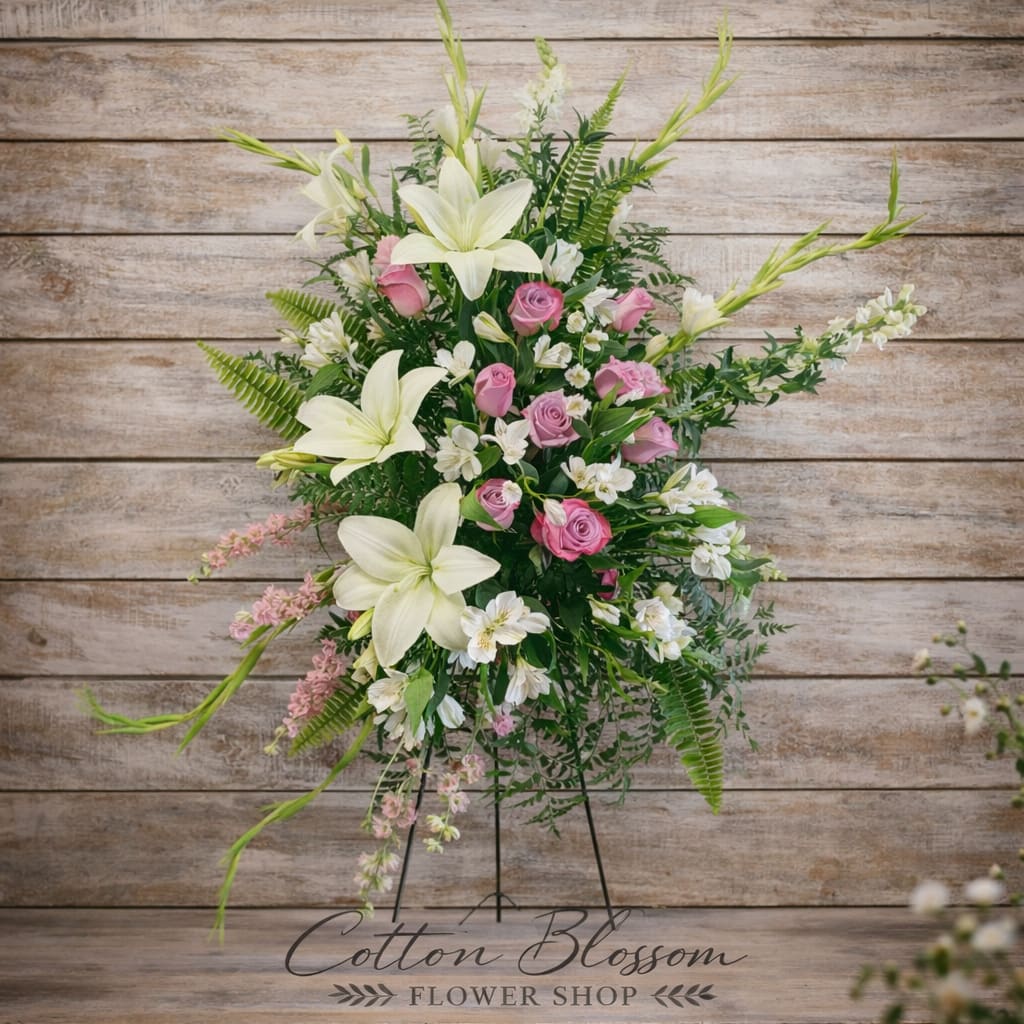 Graceful Remembrance Standing Spray - Graceful Remembrance Standing Spray – Funeral Flowers in Maricopa, AZ  Honor a beautiful life with our Graceful Remembrance Standing Spray, a soft and elegant floral tribute designed to express love, peace, and heartfelt sympathy.  This stunning arrangement features creamy white lilies, soft lavender roses, delicate alstroemeria, snapdragons, gladiolas, and seasonal accent blooms, surrounded by lush greenery and ferns. Designed on a standing easel, the spray offers a tall, flowing presentation that creates a meaningful focal point for funeral services, memorial ceremonies, or celebration of life gatherings.  The combination of white and blush tones symbolizes purity, grace, admiration, and everlasting love, making this tribute especially fitting for honoring a mother, grandmother, sister, or cherished friend.  Each arrangement is hand-crafted in Cotton Blossom’s signature style using premium, fresh flowers for a full and balanced display.  Cotton Blossom Flower Shop proudly provides same-day sympathy and funeral flower delivery in Maricopa, Casa Grande, and Stanfield, Arizona. Trust your local Maricopa florist to deliver a beautiful and respectful tribute when it matters most.