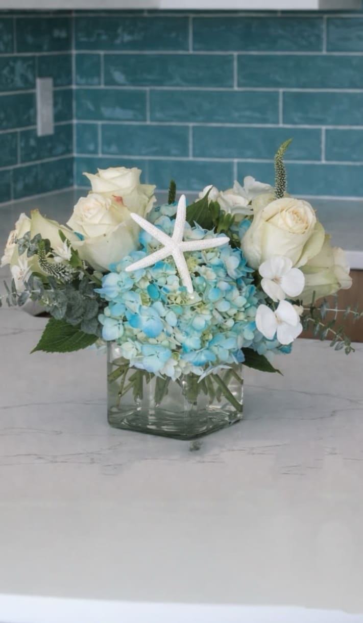 Studio K Signature Beach Bouquet™ - A serene mix of creamy white roses and blue hydrangea with delicate white blooms and fresh greenery—designed to feel light, calm, and coastal.  Each piece is Designer’s Choice, created with fresh seasonal blooms. Flowers and colors may vary based on availability while maintaining the overall style and quality.   Better for: Anniversary, Thank You, Get Well, New Baby, Housewarming, Thinking of You, Just Because, New Home