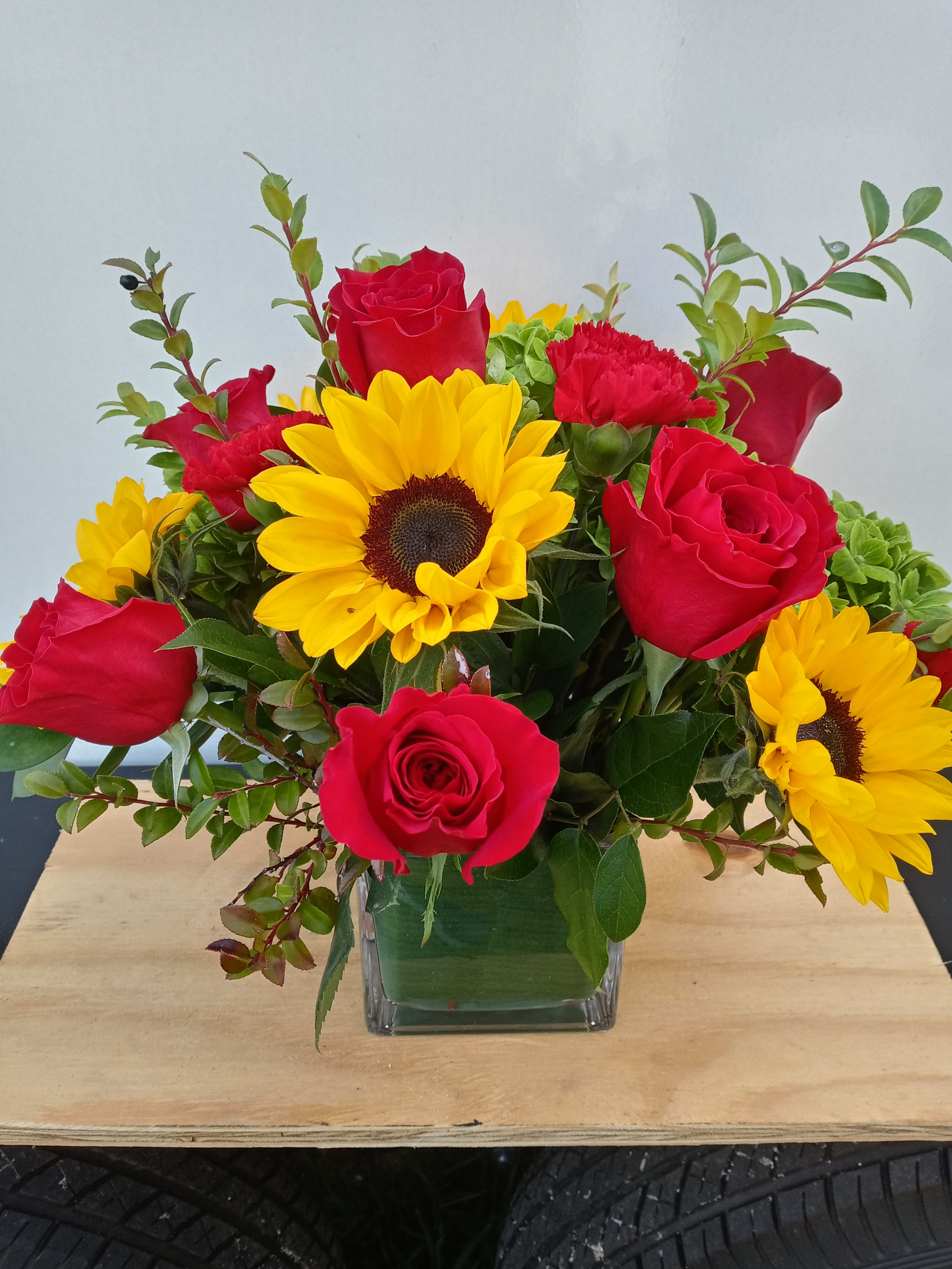 Sunflowers and roses - Sunflowers, red roses, carnations and green hydrangea arranged in a 5 "x 5" glass cube.