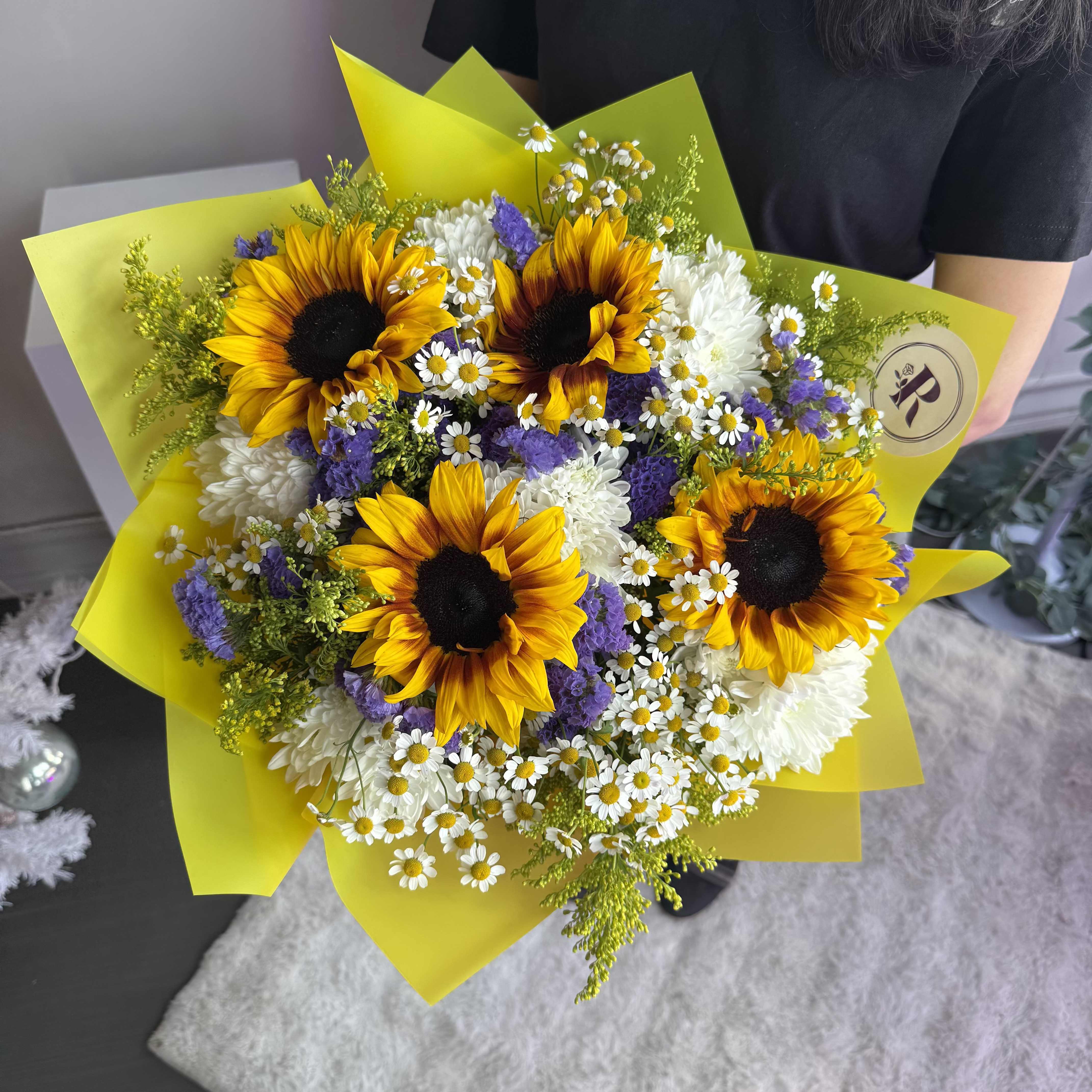 69P- Sunny Bouquet - Bring sunshine into someone's life with this vibrant sunflower bouquet. Bursting with bright yellow sunflowers, delicate white daisies, and rich purple accents, this stunning arrangement is wrapped in soft yellow paper to enhance its cheerful, radiant look. Perfect for birthdays, anniversaries, or any celebration, this fresh sunflower bouquet adds a pop of color and joy to any occasion. The Premium size is shown in the picture.