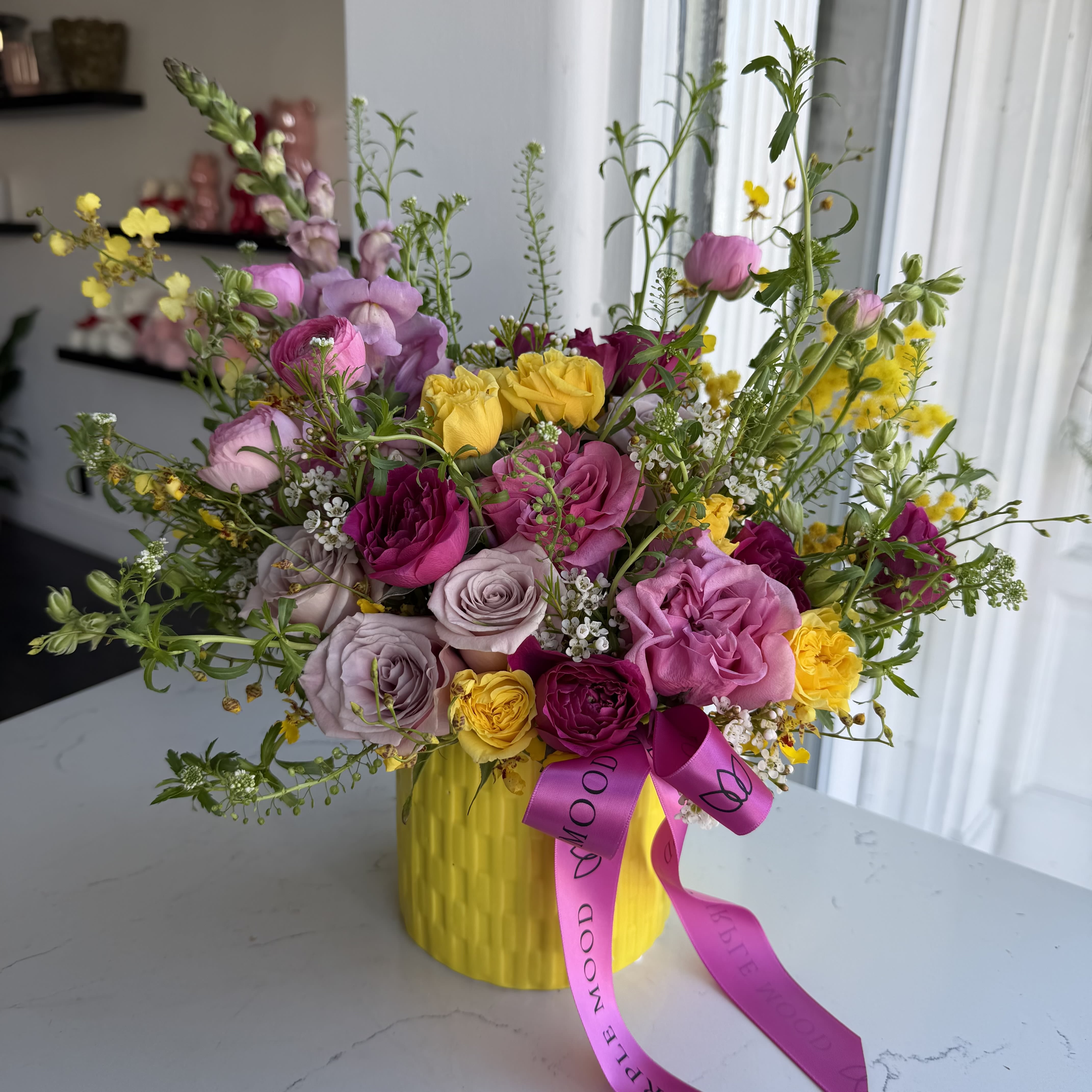 Lemonade Vase - A joyful garden-style arrangement bursting with vibrant pink and yellow blooms, delicate seasonal florals, and fresh greenery. Designed in our signature yellow vase and finished with a Purple Mood ribbon, this arrangement brings sunshine and color to any room. Playful yet refined, it’s the perfect statement for birthdays, celebrations, or just because.