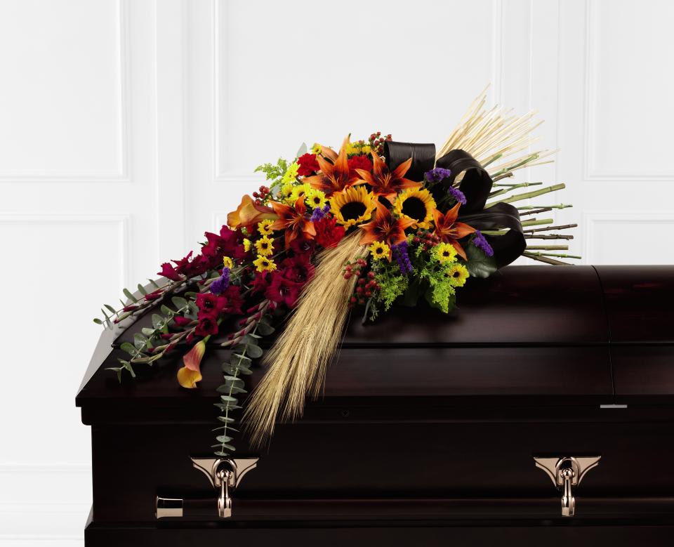 FTD Glorious Garden Casket Spray - The FTD Glorious Garden Casket Spray has a sweeping look that   will add to the elegance and sophistication of their final farewell   service.  Burgundy gladiolus, orange Asiatic lilies, orange mini calla   lilies, purple statice, red carnations, sunflowers, solidago, viking   bi-colored chrysanthemums, burgundy ti leaves, baby blue eucalyptus,   lush greens and dried wheat stems are beautifully brought together to   create a graceful arrangement that honors the life of the deceased with   every beautiful bloom.    0"h x 45"w
