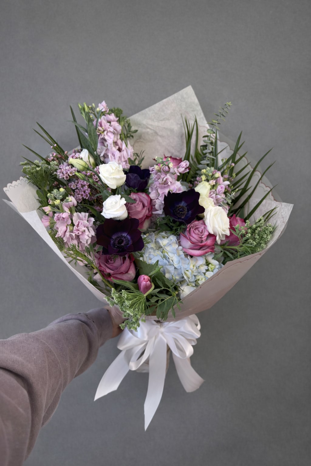  Garden Luxe Bouquet - Celebrate Mom with a lush, garden-inspired bouquet designed in soft, elegant tones. This hand-tied arrangement features premium roses, delicate stock, hydrangea, striking anemones, and fresh seasonal blooms, all beautifully wrapped and finished with a satin ribbon. Full, feminine, and luxurious — the perfect way to say thank you for everything, Mom. Each bouquet is crafted fresh with the finest flowers of the season, creating a memorable and elegant Mother's Day gift she will truly love.